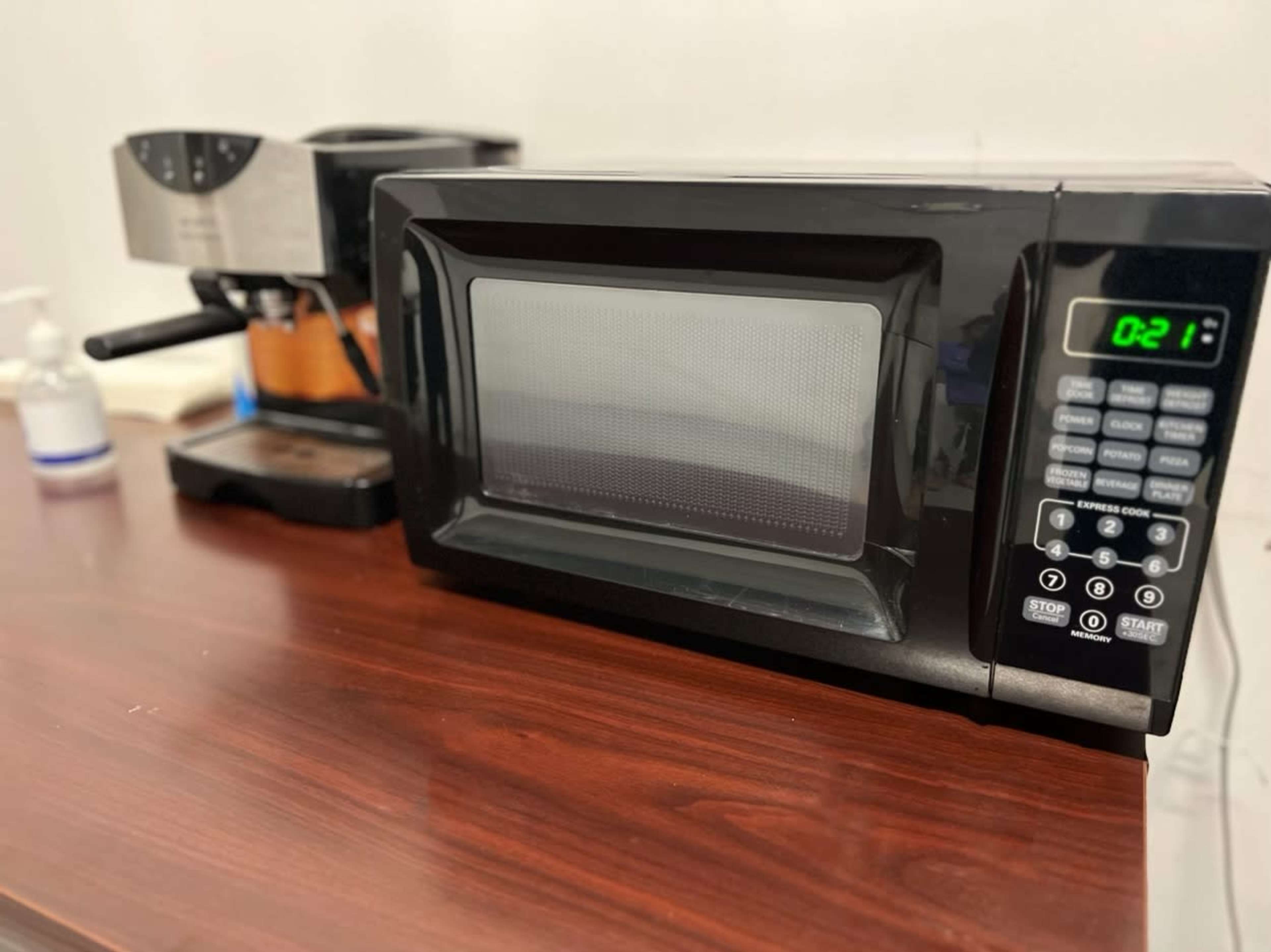 A black microwave is placed on a wooden table next to a coffee maker.