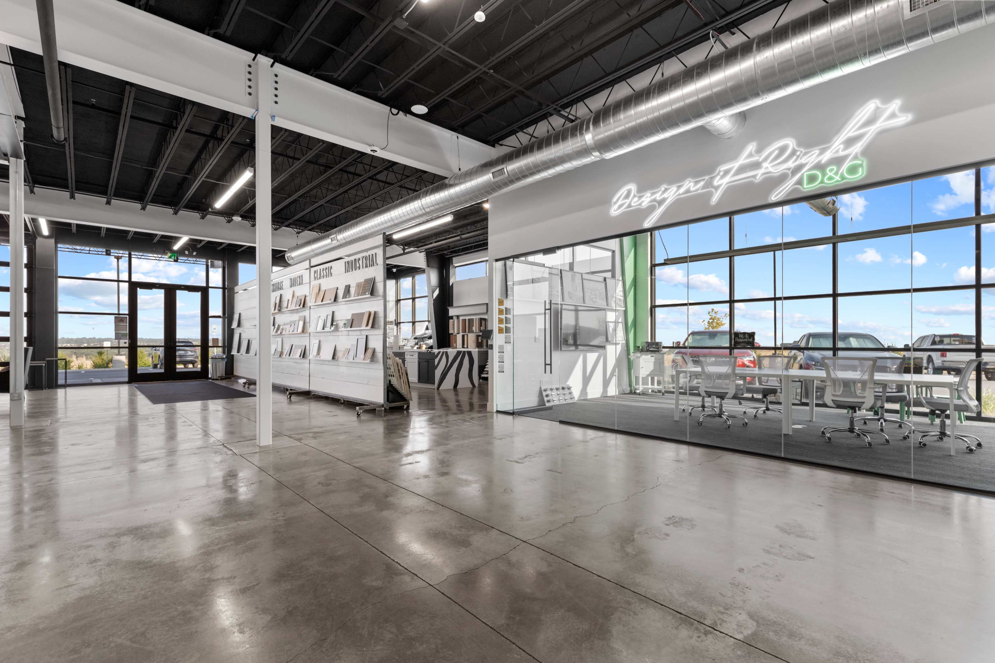 The image shows a spacious modern office interior with large windows, polished concrete floors, and a glass-walled meeting space.