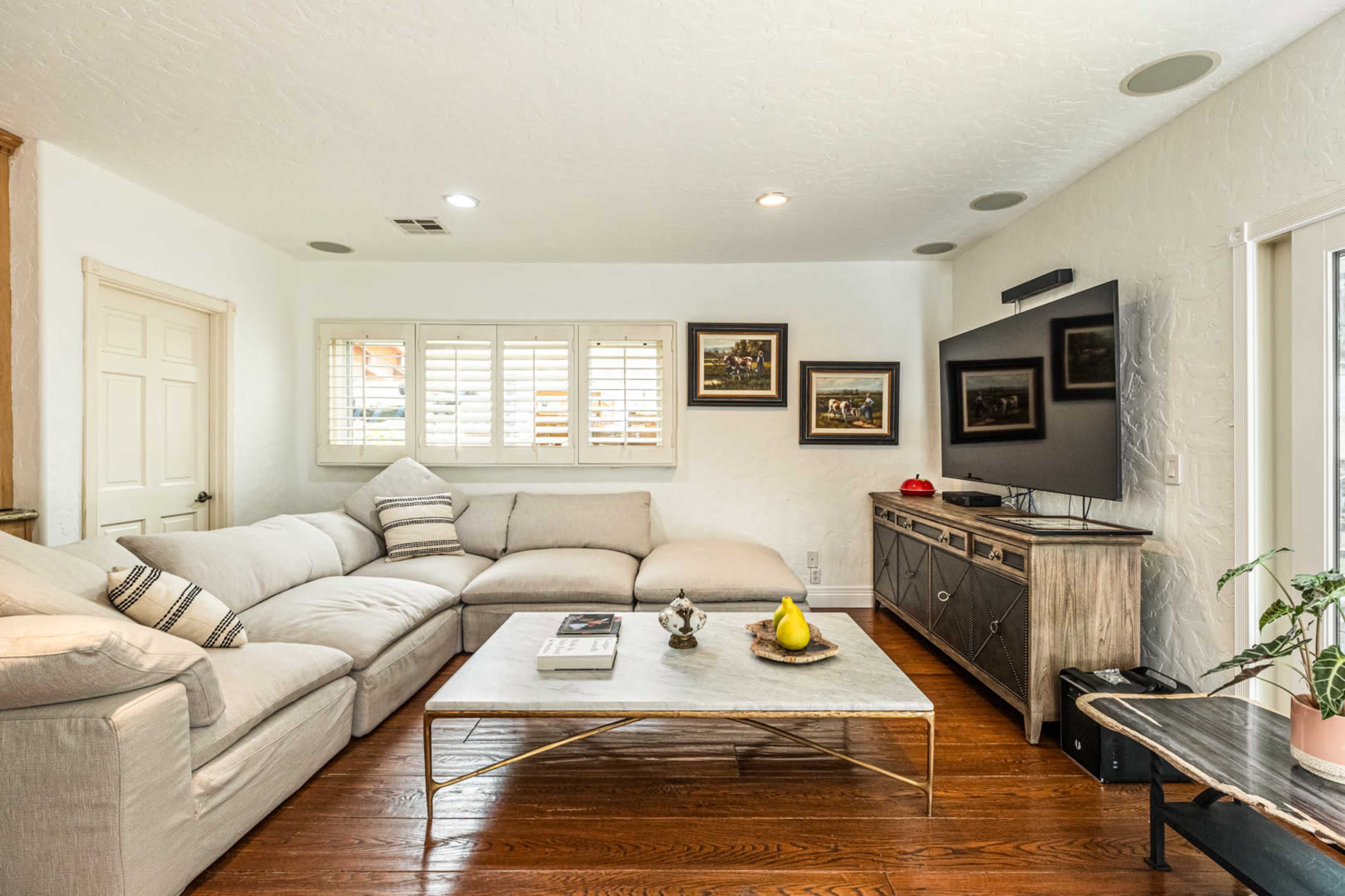 A modern living room features a large sectional sofa, a coffee table with decorative items, and a wall-mounted TV.