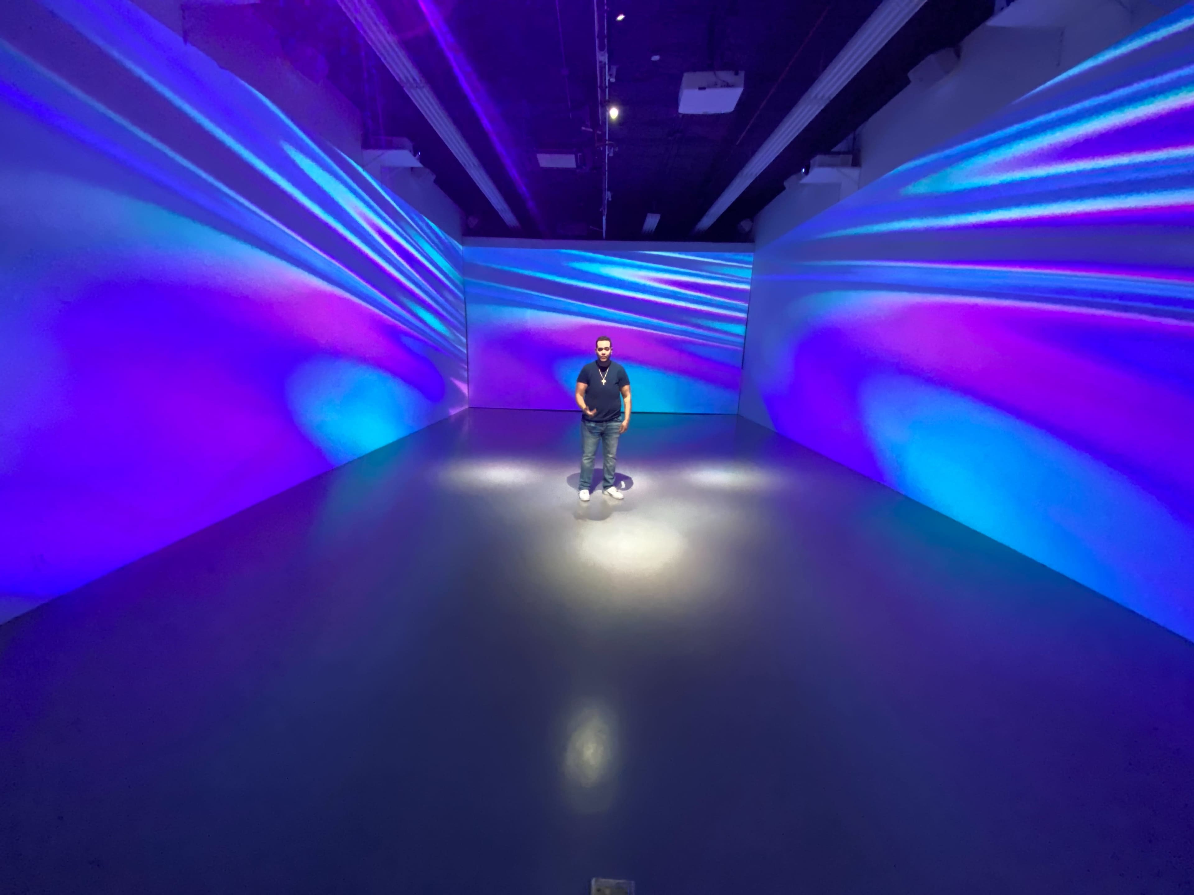 A person stands in a dimly lit room with vibrant blue and purple light projections on the walls.