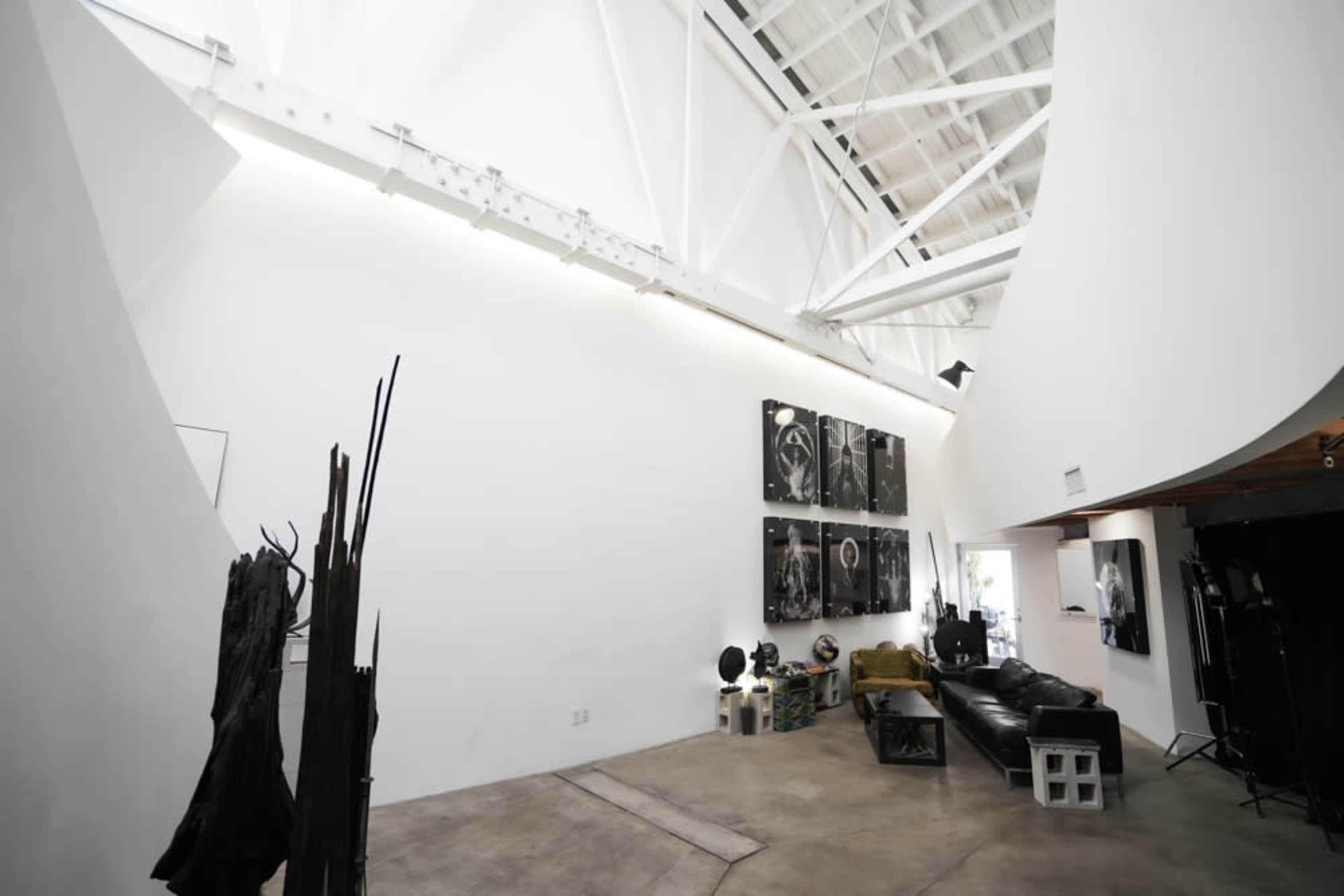 A spacious, modern interior with high white walls, exposed beams, and a minimalist design featuring artwork and sculptures.