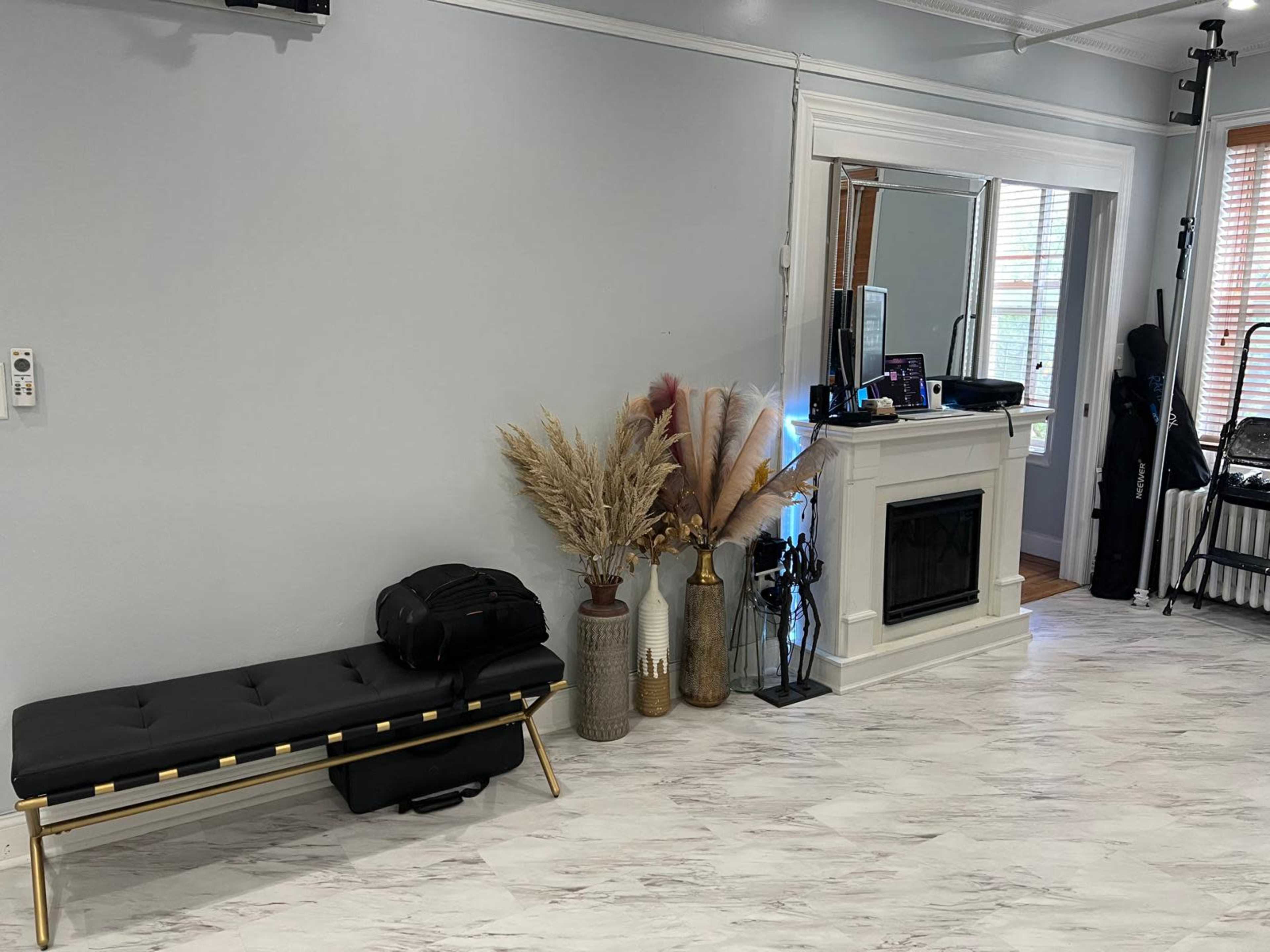 The image shows a room with a bench, decorative plants, a mirror, and a fireplace, along with various equipment and bags placed nearby.