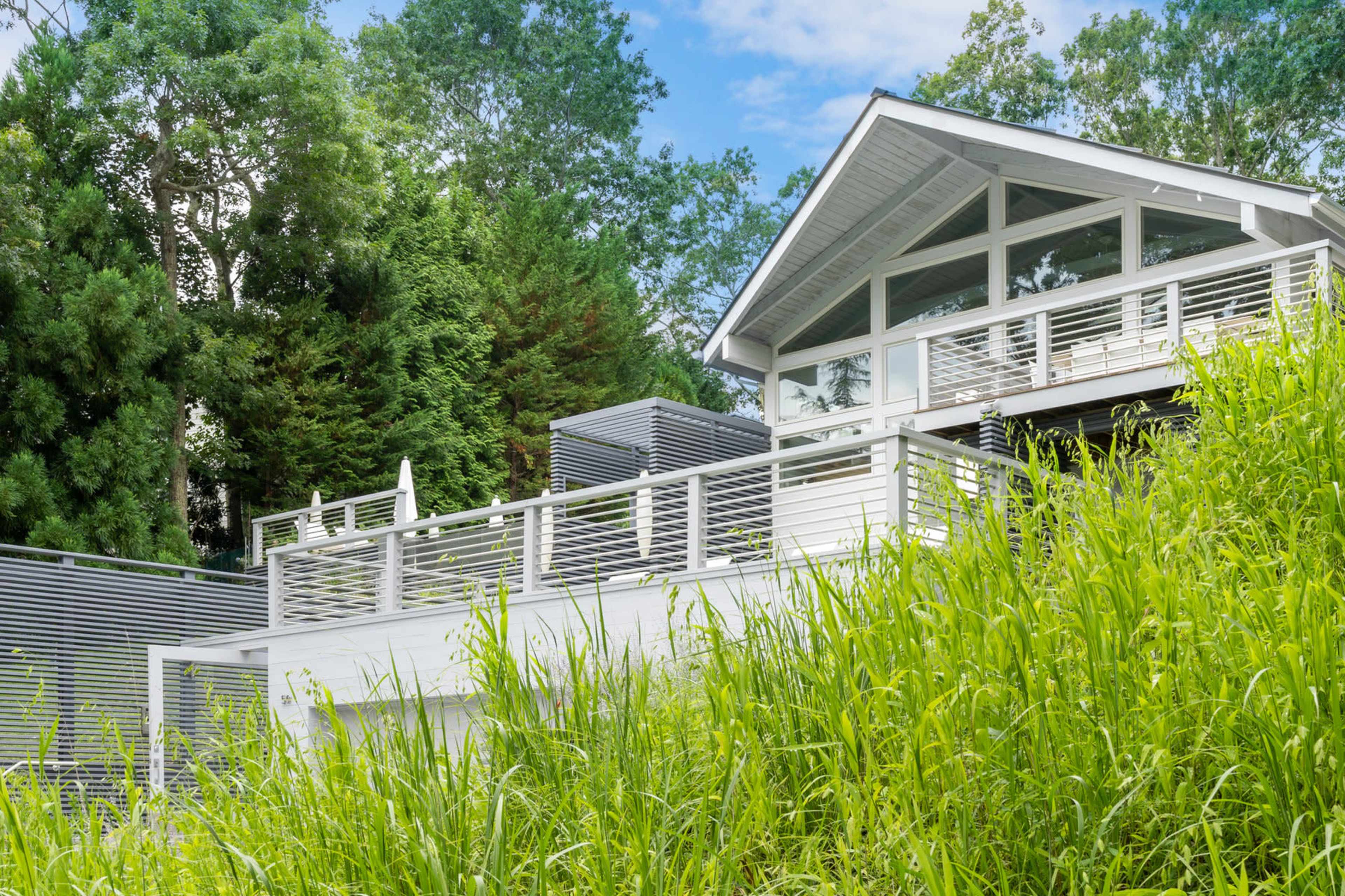 A modern white house with a sloped roof and a deck overlooks a lush green landscape.