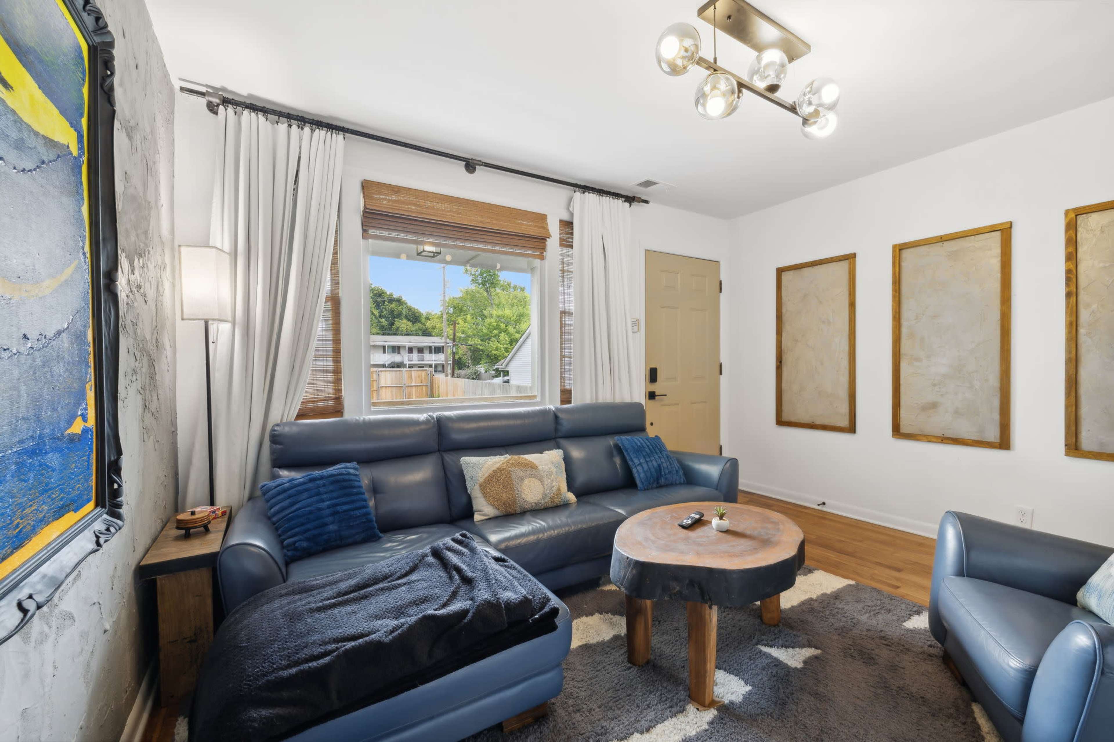 The image shows a living room with a blue leather sofa, a wooden coffee table, and three framed artworks on the wall.