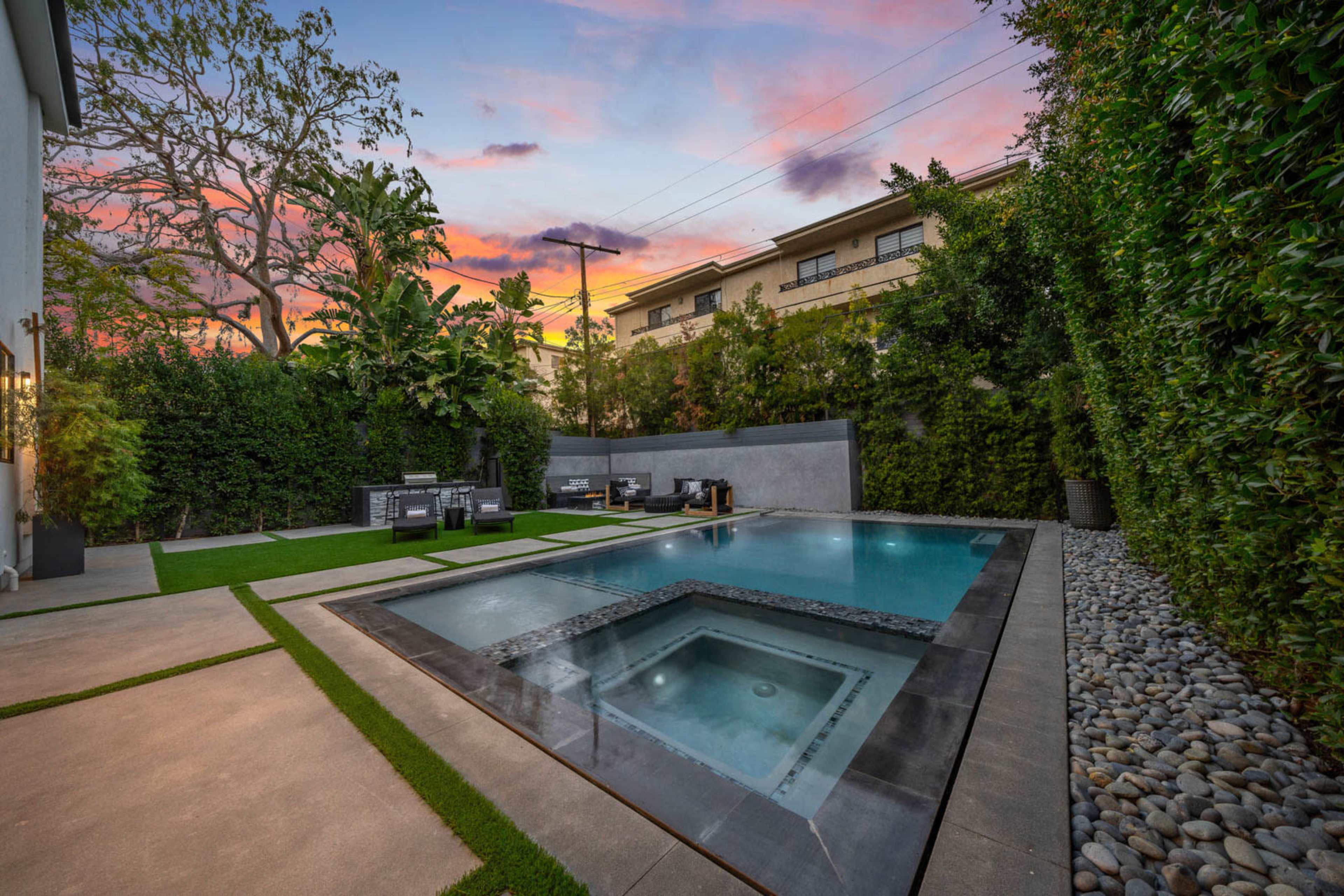 A modern backyard featuring a swimming pool with a hot tub, surrounded by neatly landscaped greenery and outdoor seating.