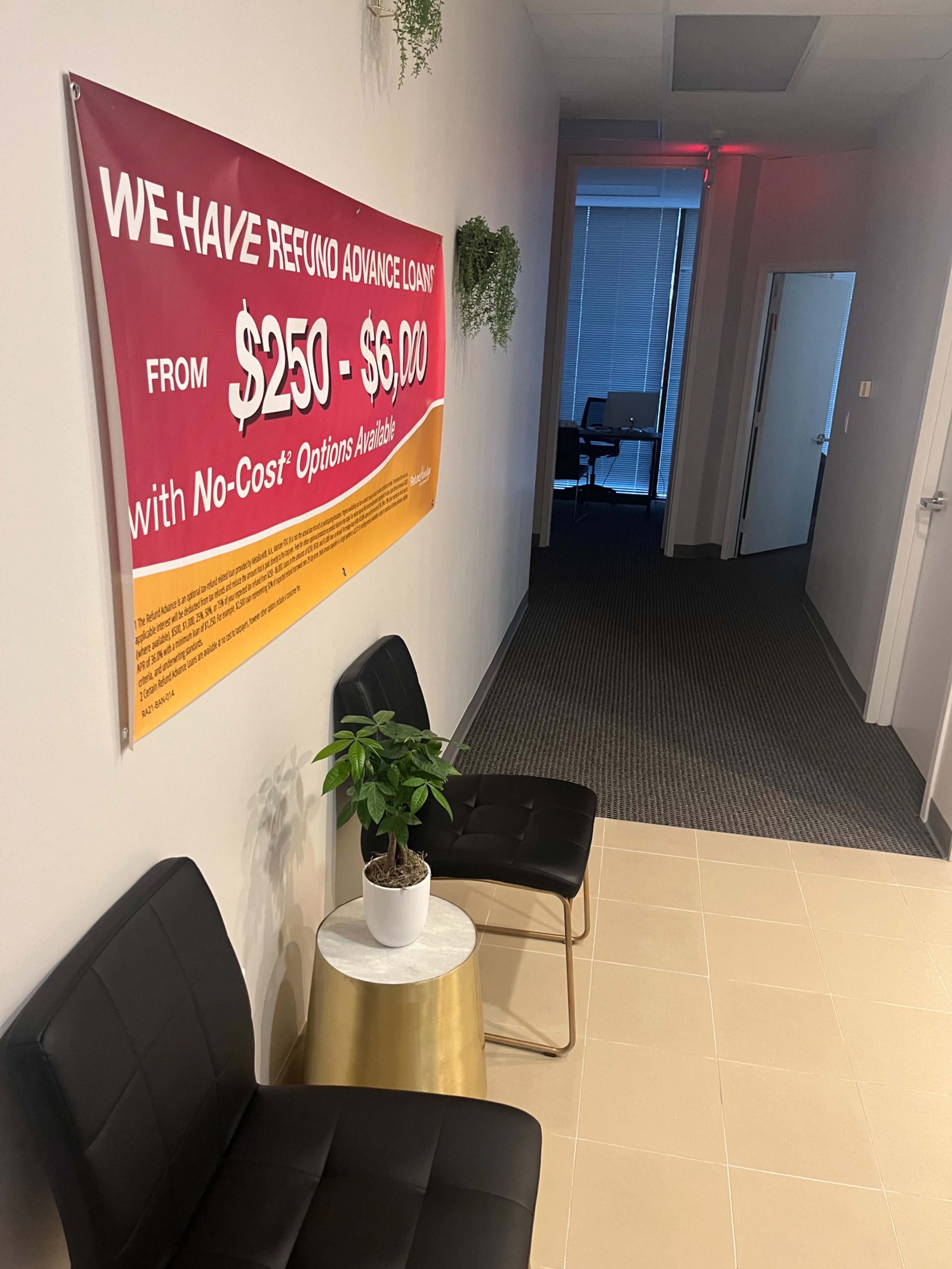 The image shows a hallway featuring a banner advertising refund advance loans, two black chairs, a small plant on a gold table, and a bright window in the background.