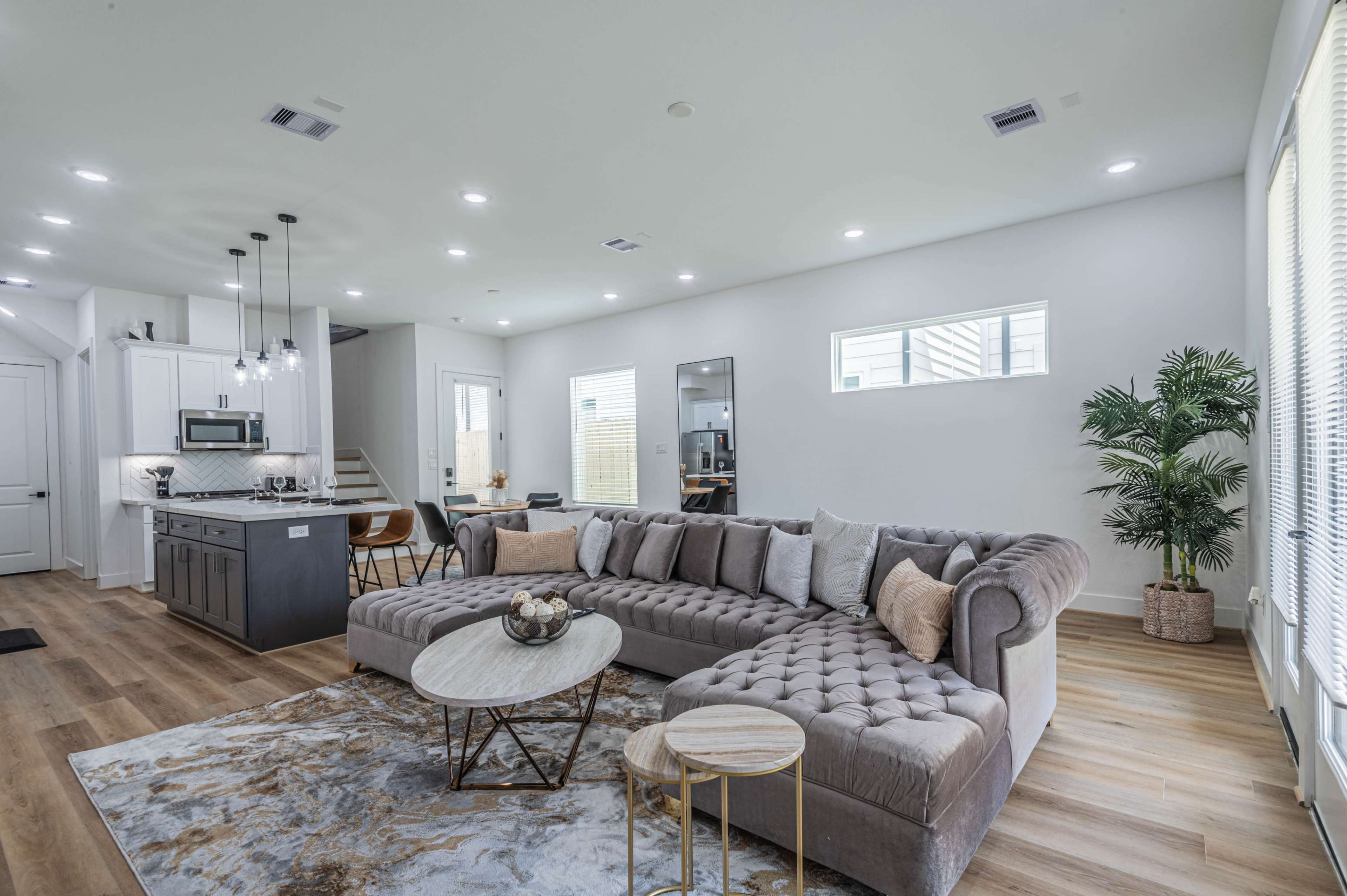 A modern living room with a large gray sectional sofa, a round coffee table, and a dining area visible in the background.