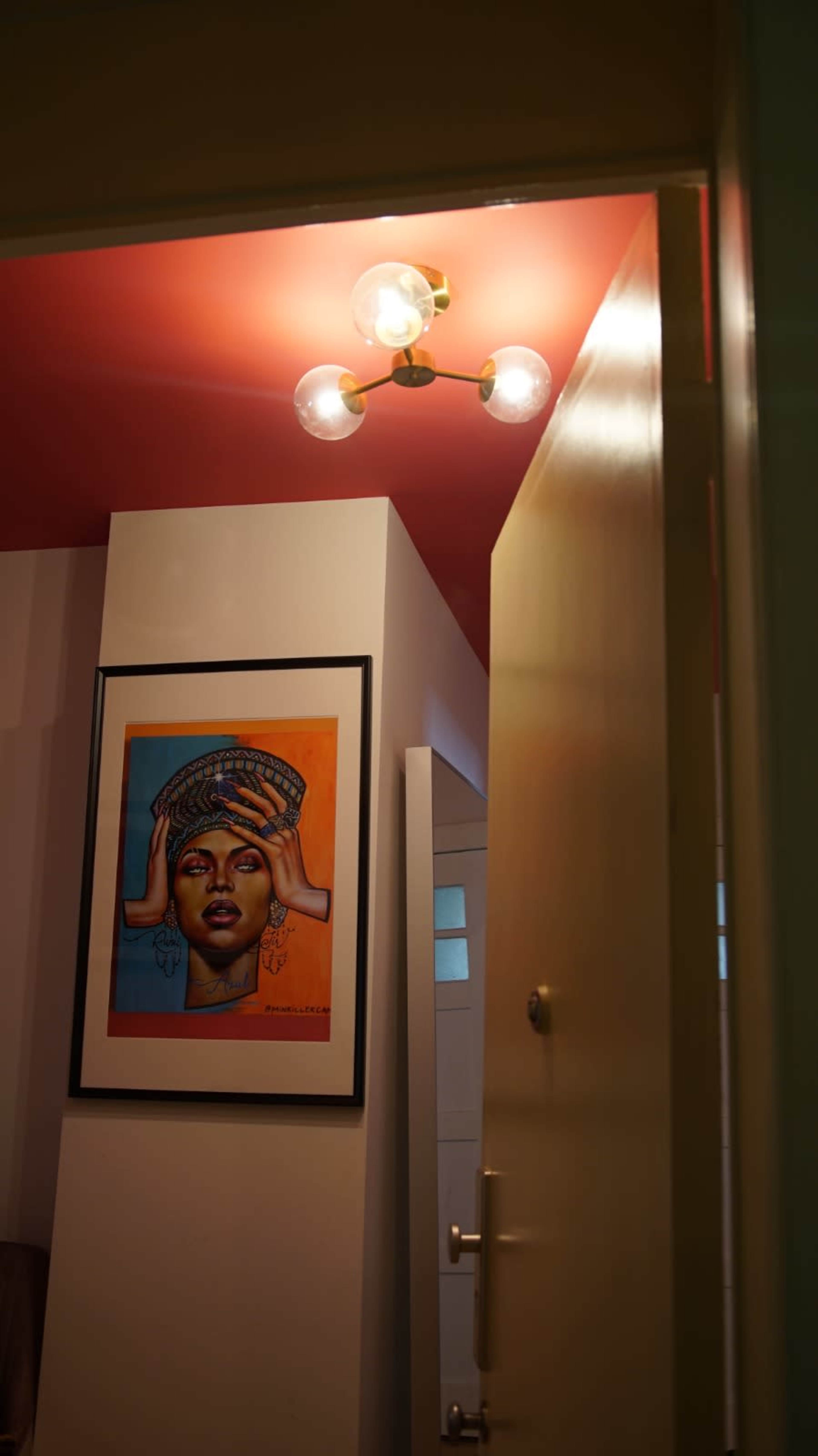 A brightly colored room is partially visible through an open door, featuring a framed artwork of a woman on the wall and a modern light fixture overhead.