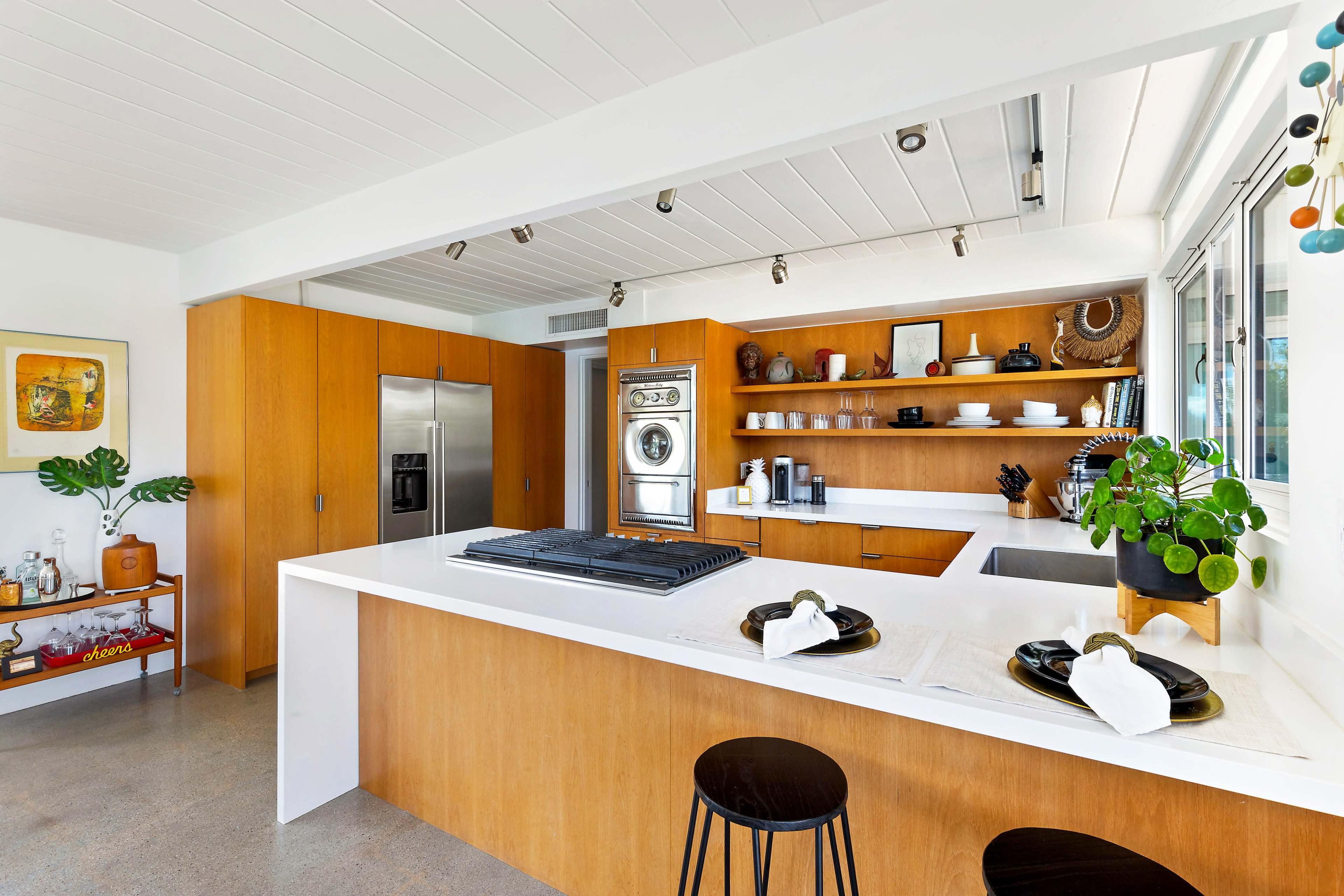 The image shows a modern kitchen featuring wooden cabinetry, stainless steel appliances, and a central island with a cooktop.