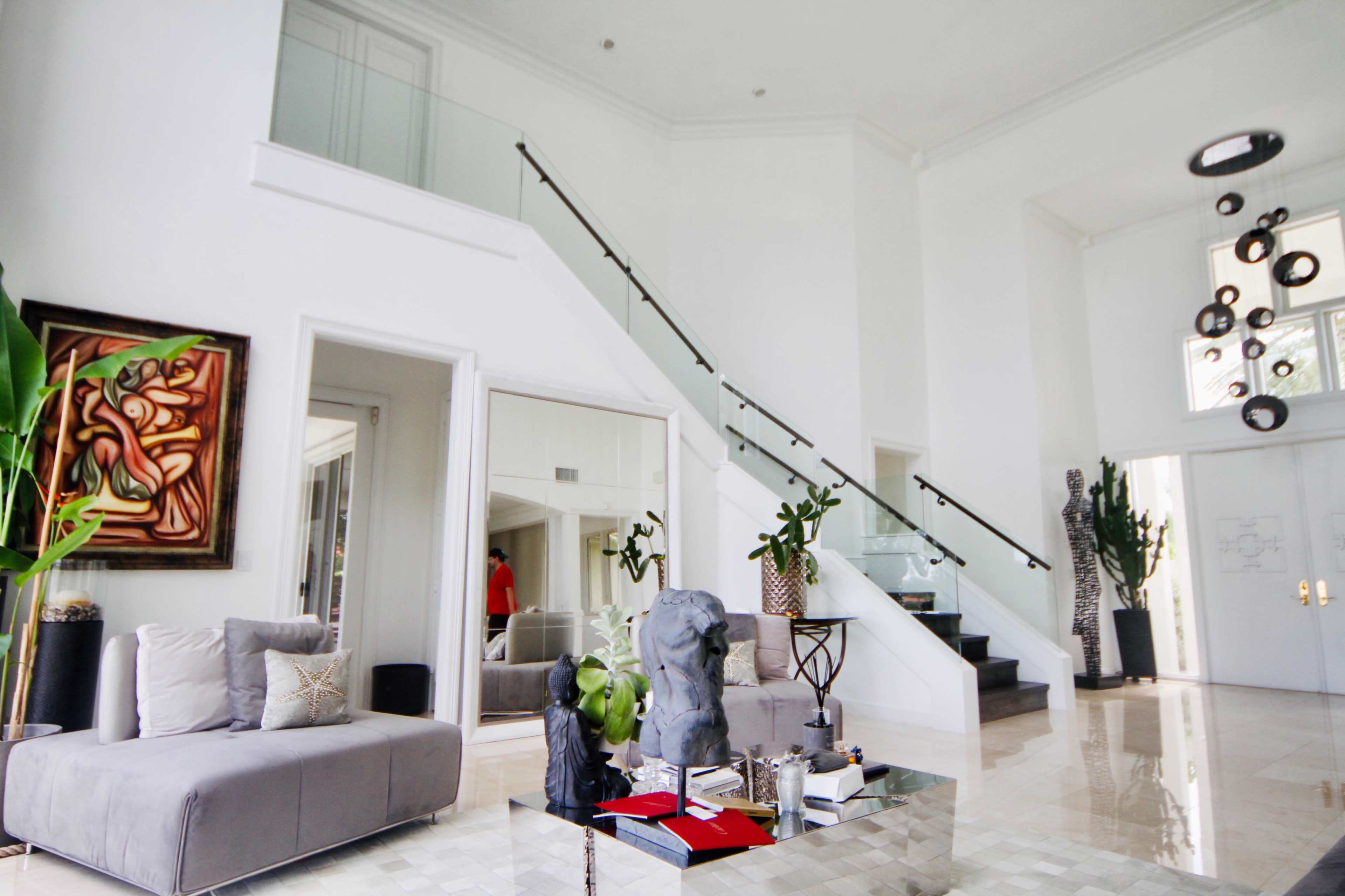 The interior of a modern home features a spacious living area with a gray sofa, a staircase leading to an upper level, and large windows allowing natural light to enter.