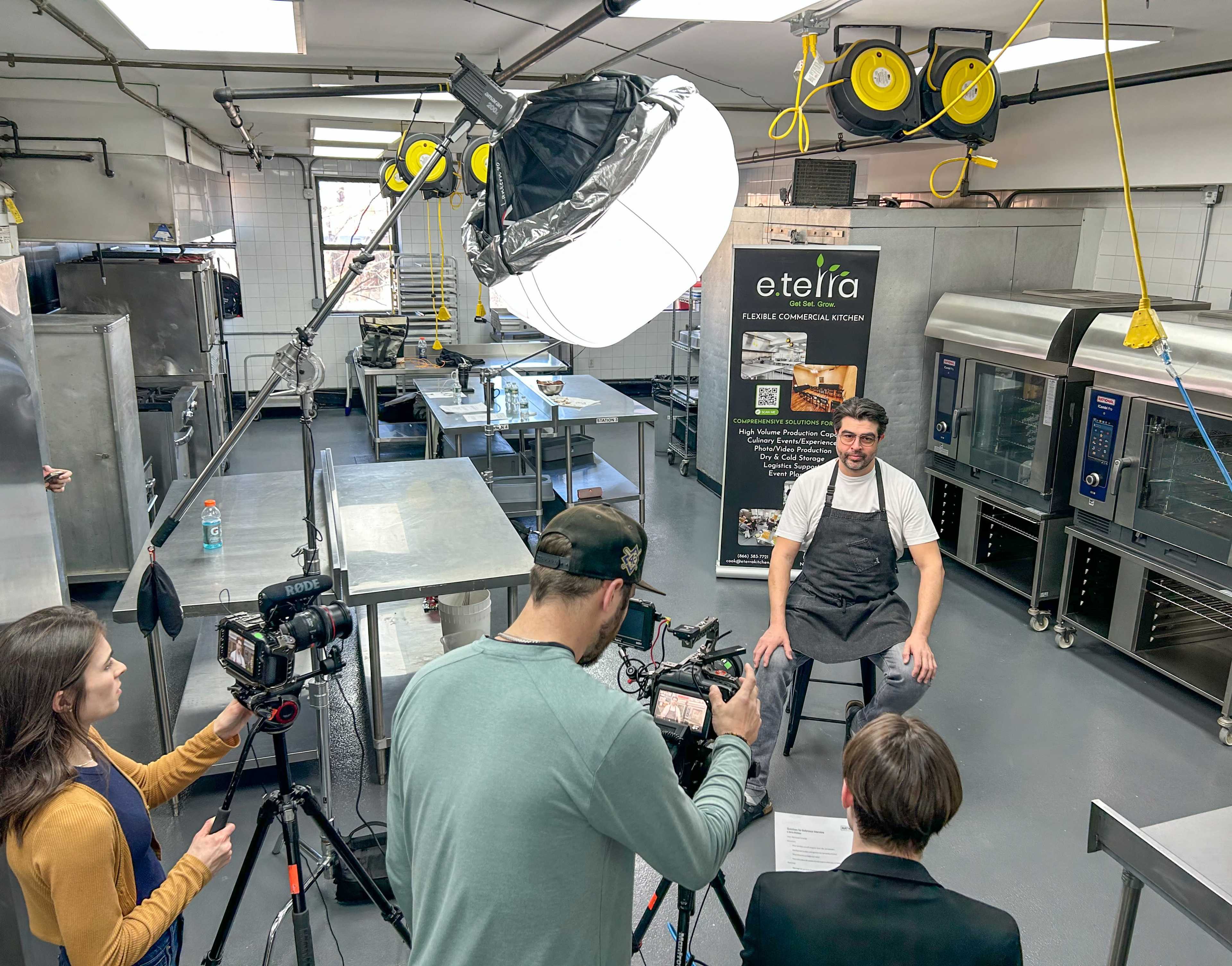 A chef sits in a commercial kitchen while a small film crew prepares to interview him.