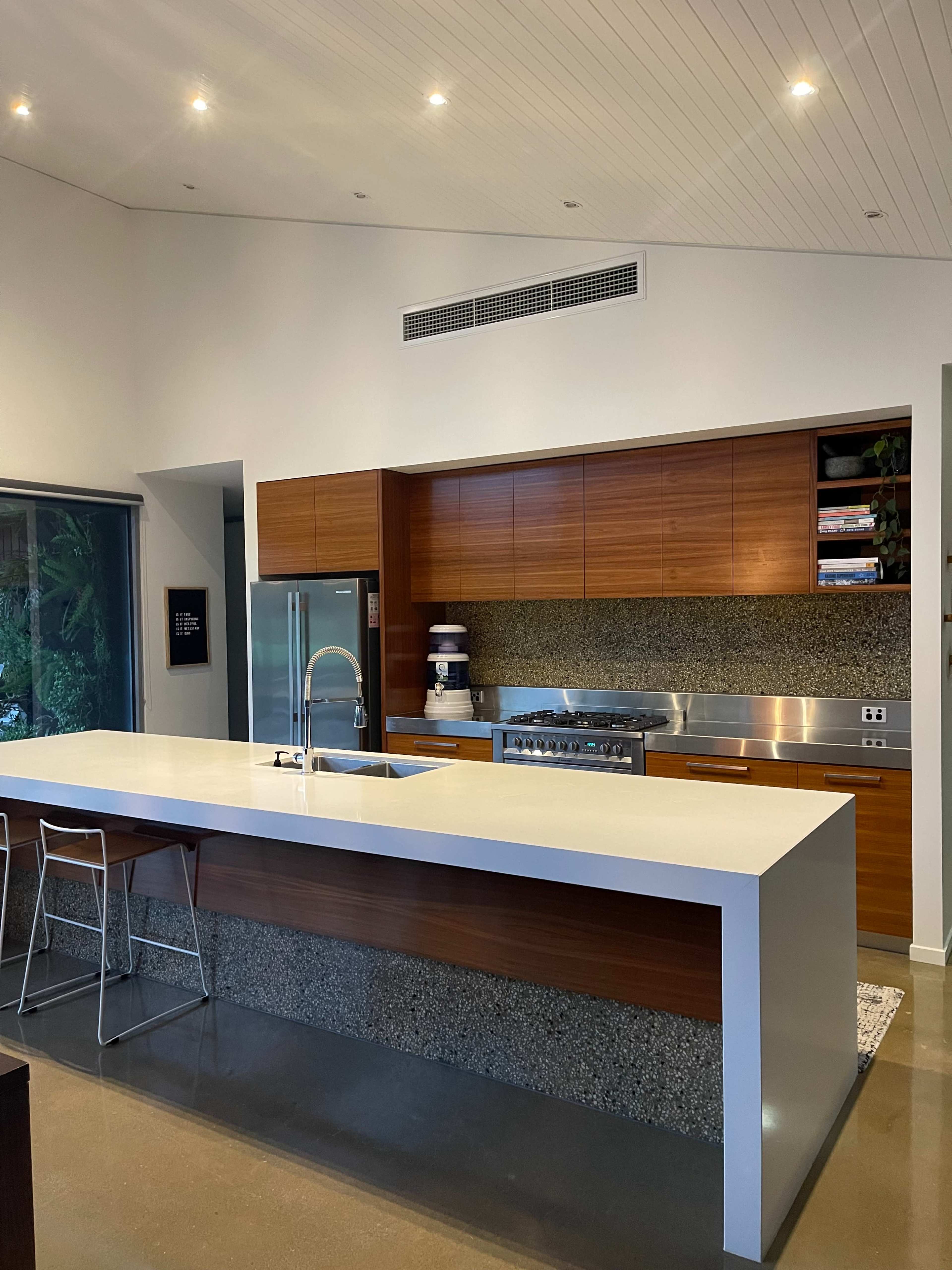 The image shows a modern kitchen with a large white island, wooden cabinetry, and stainless steel appliances.