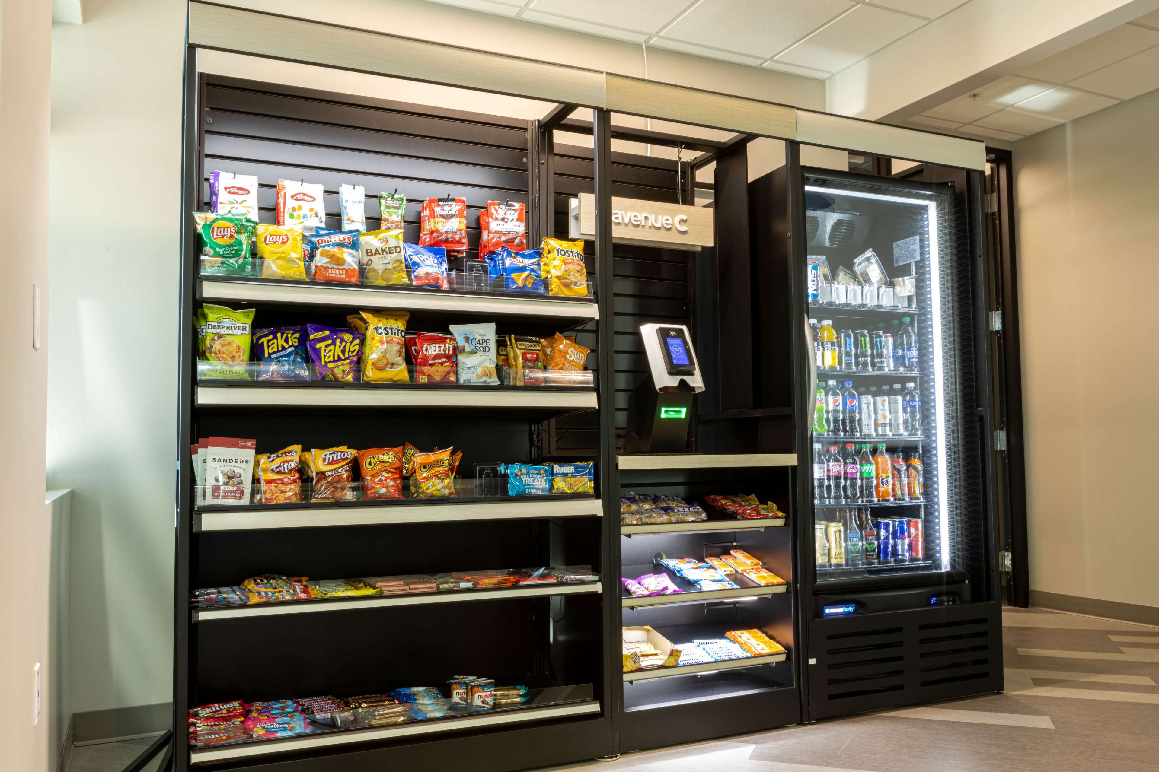 The image shows a vending machine setup with shelves stocked with various snacks and beverages in a well-lit room.