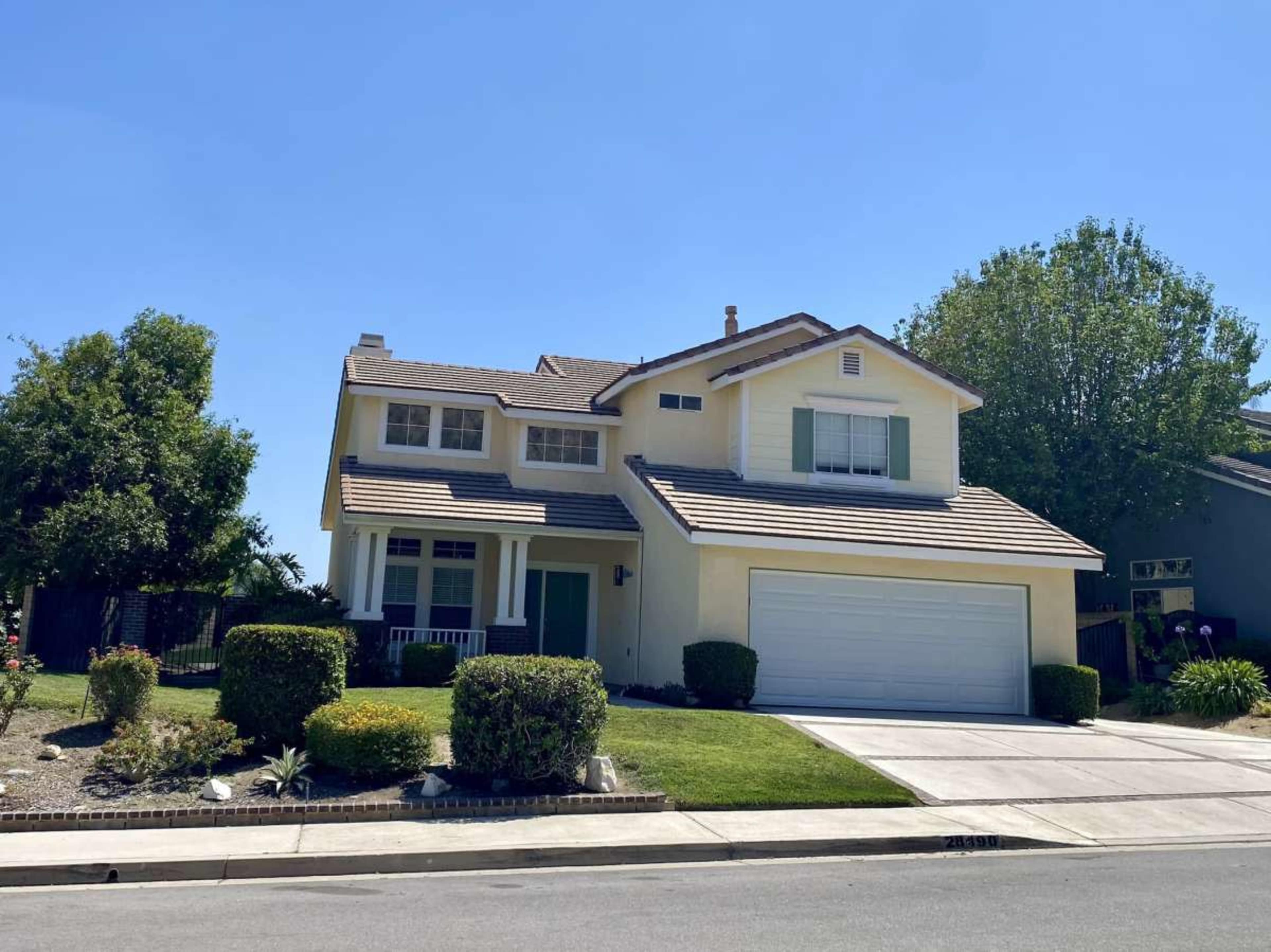 The image shows a two-story yellow house with a front lawn and driveway on a clear day.