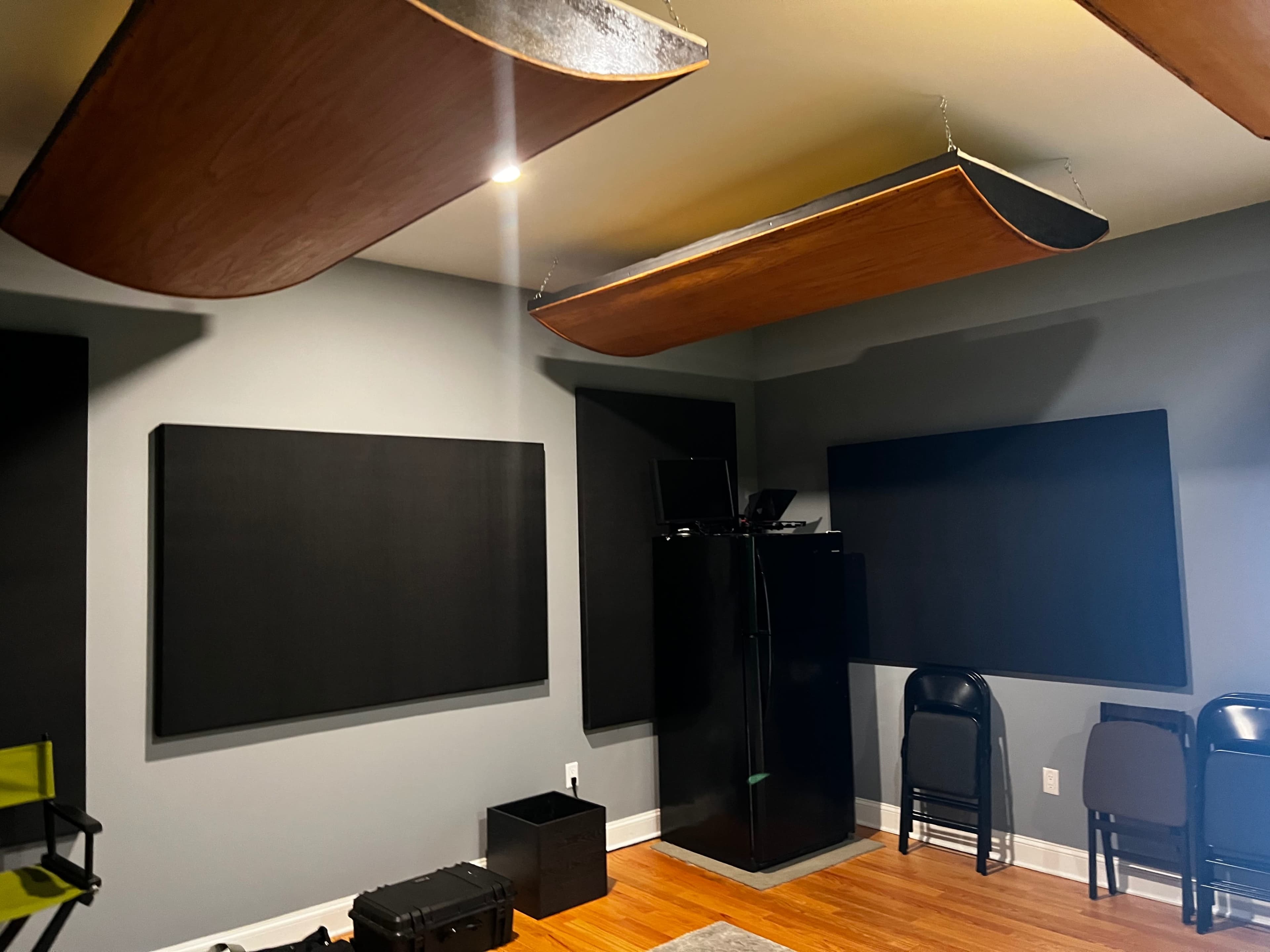 A room with soundproofing panels on the walls, a black refrigerator, and several folding chairs stacked in the corner.