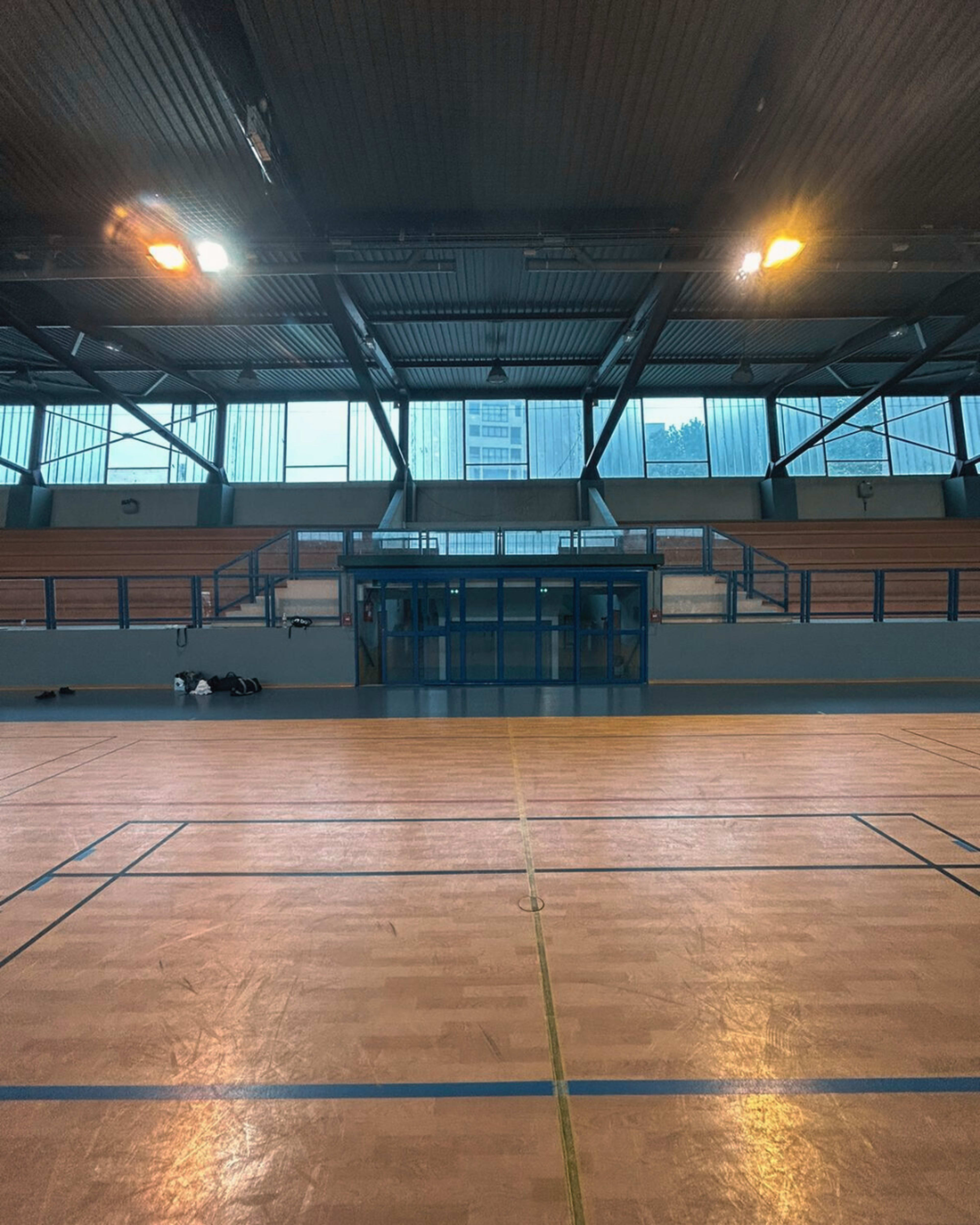 An indoor sports hall with a wooden floor and large windows letting in natural light.