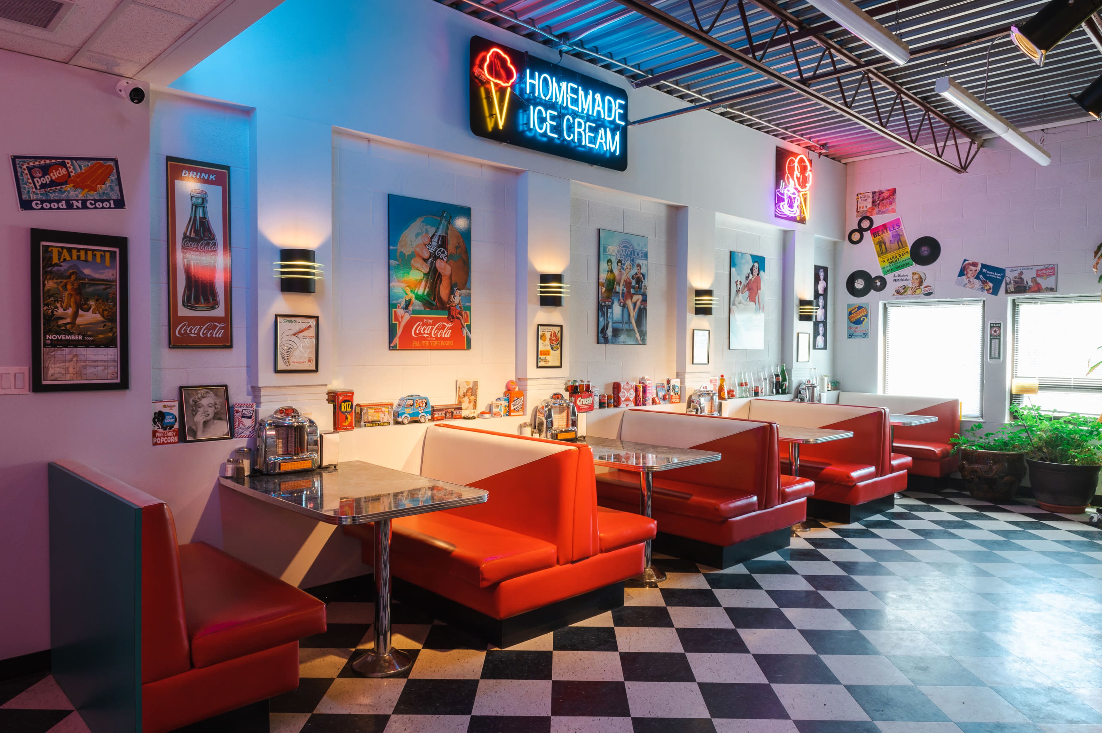 A retro diner with red booths, a checkered floor, and neon signs advertising homemade ice cream.