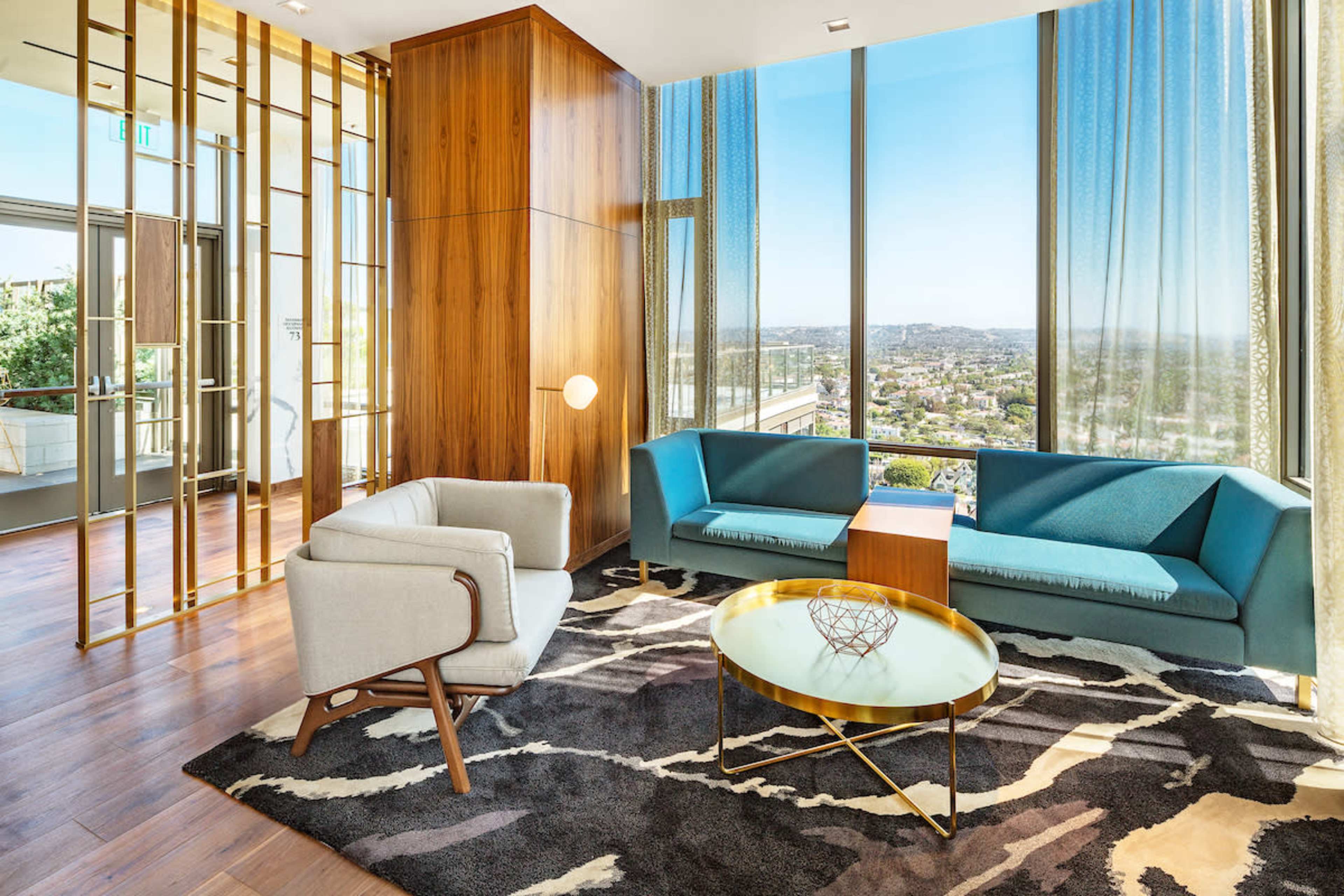 A modern lounge area with blue and gray furniture, large windows, and wooden accents, overlooking a cityscape.