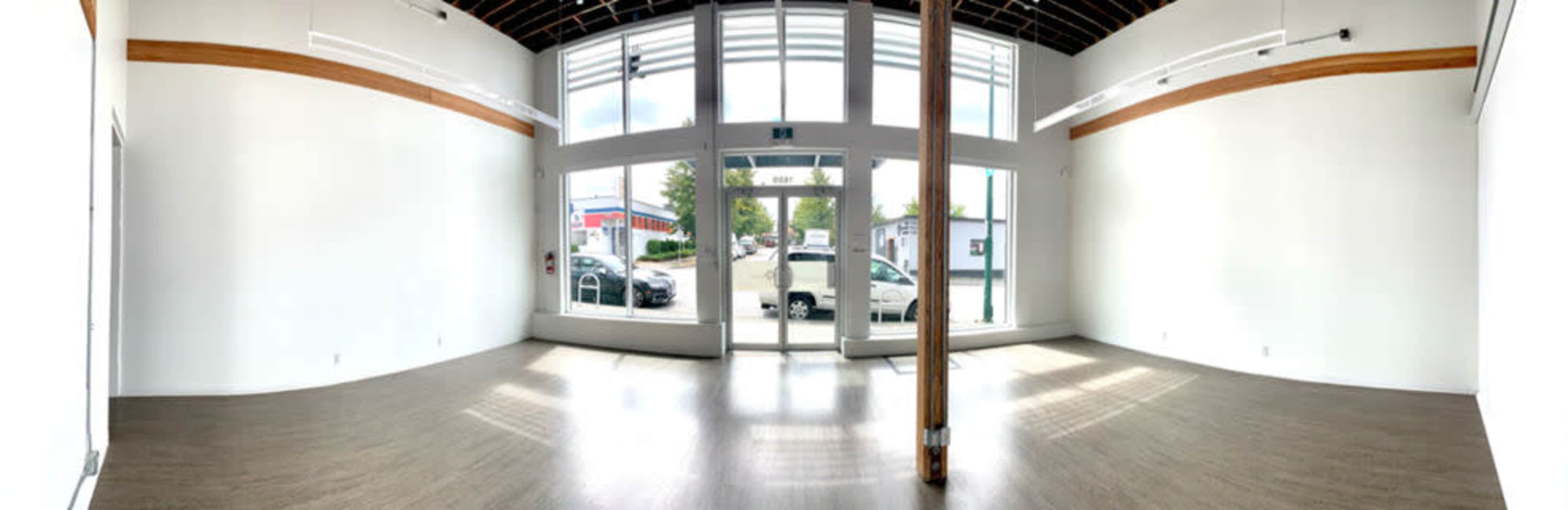 An empty commercial space with large windows, a wooden beam, and light-colored walls.
