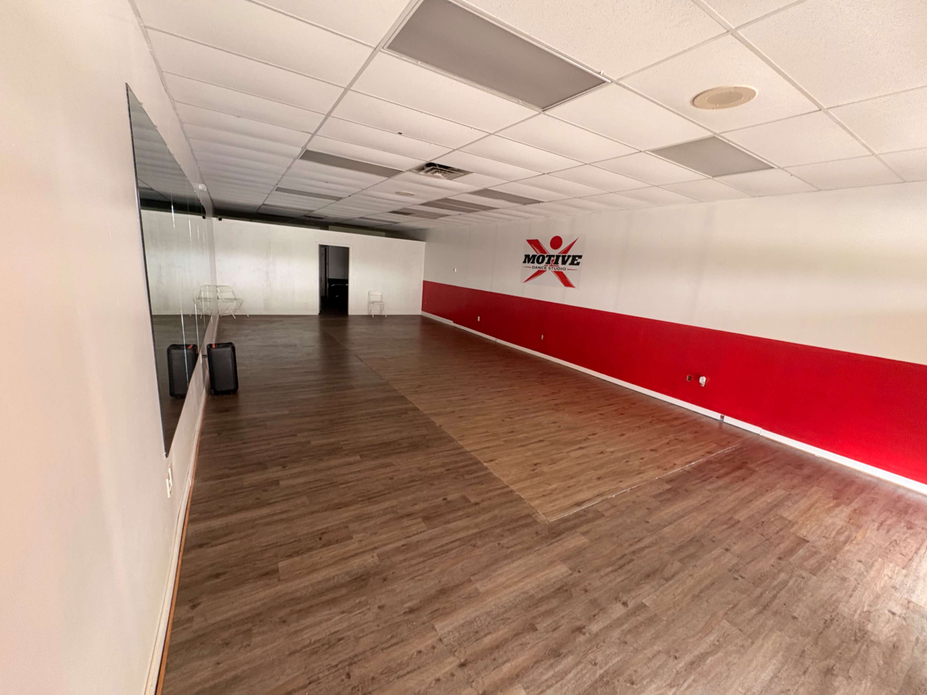 The interior of the room features a wooden floor with a red accent wall, mirrors on one side, and minimal furniture.