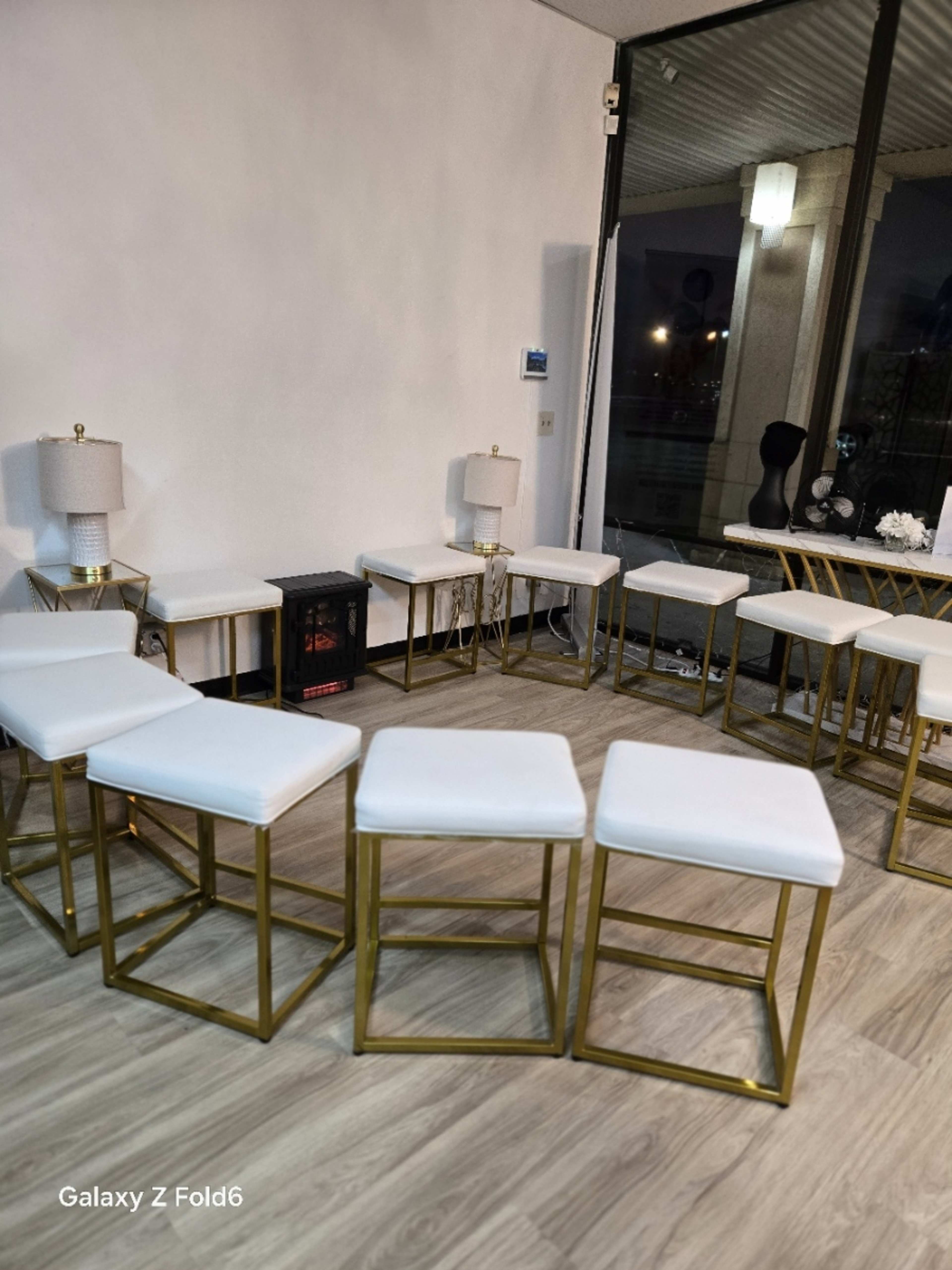 The image shows a modern interior space with a circular arrangement of white stools and two lamps beside a window.