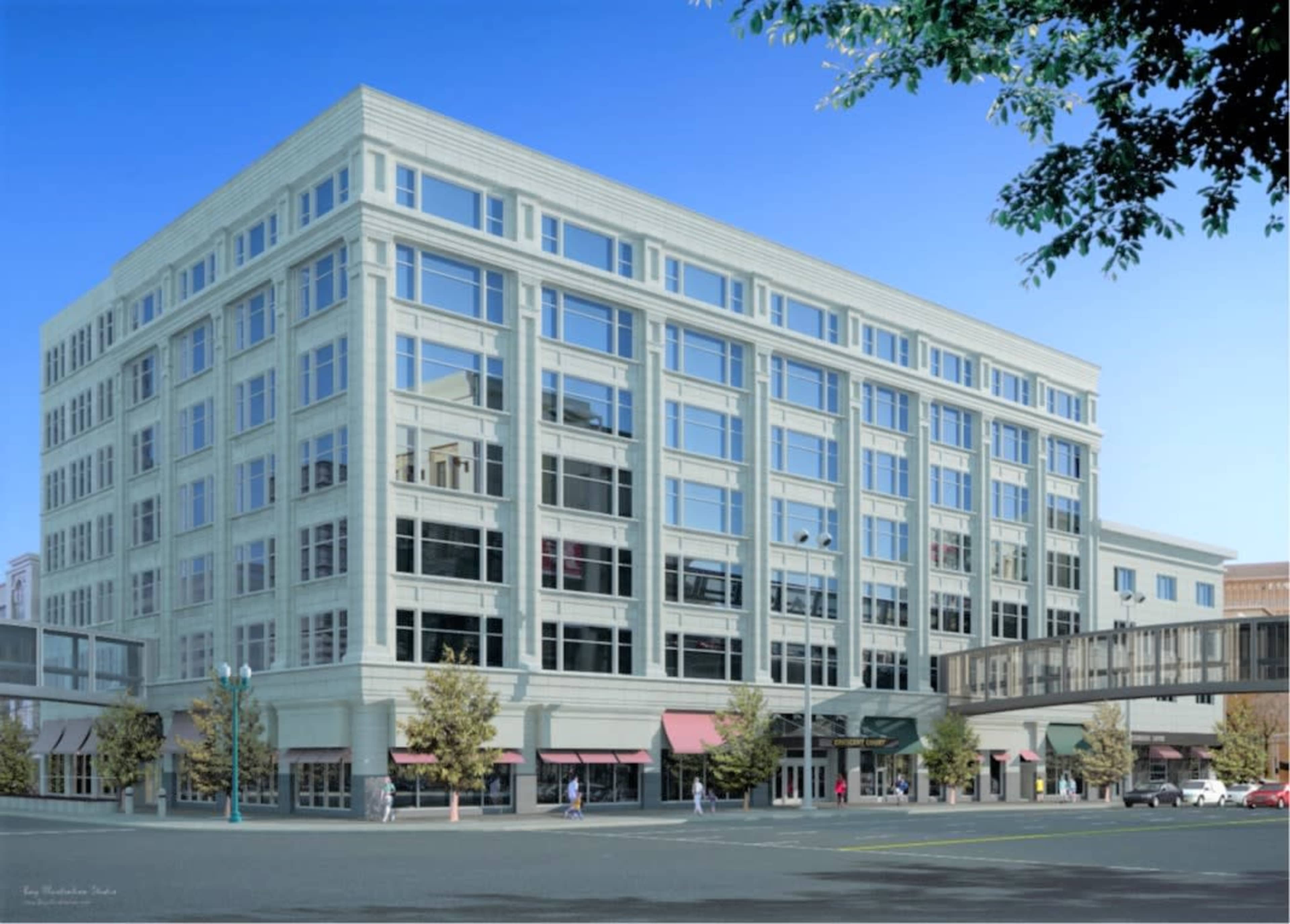 A large, modern, multi-story building with numerous windows and a pedestrian overpass, situated in an urban environment.