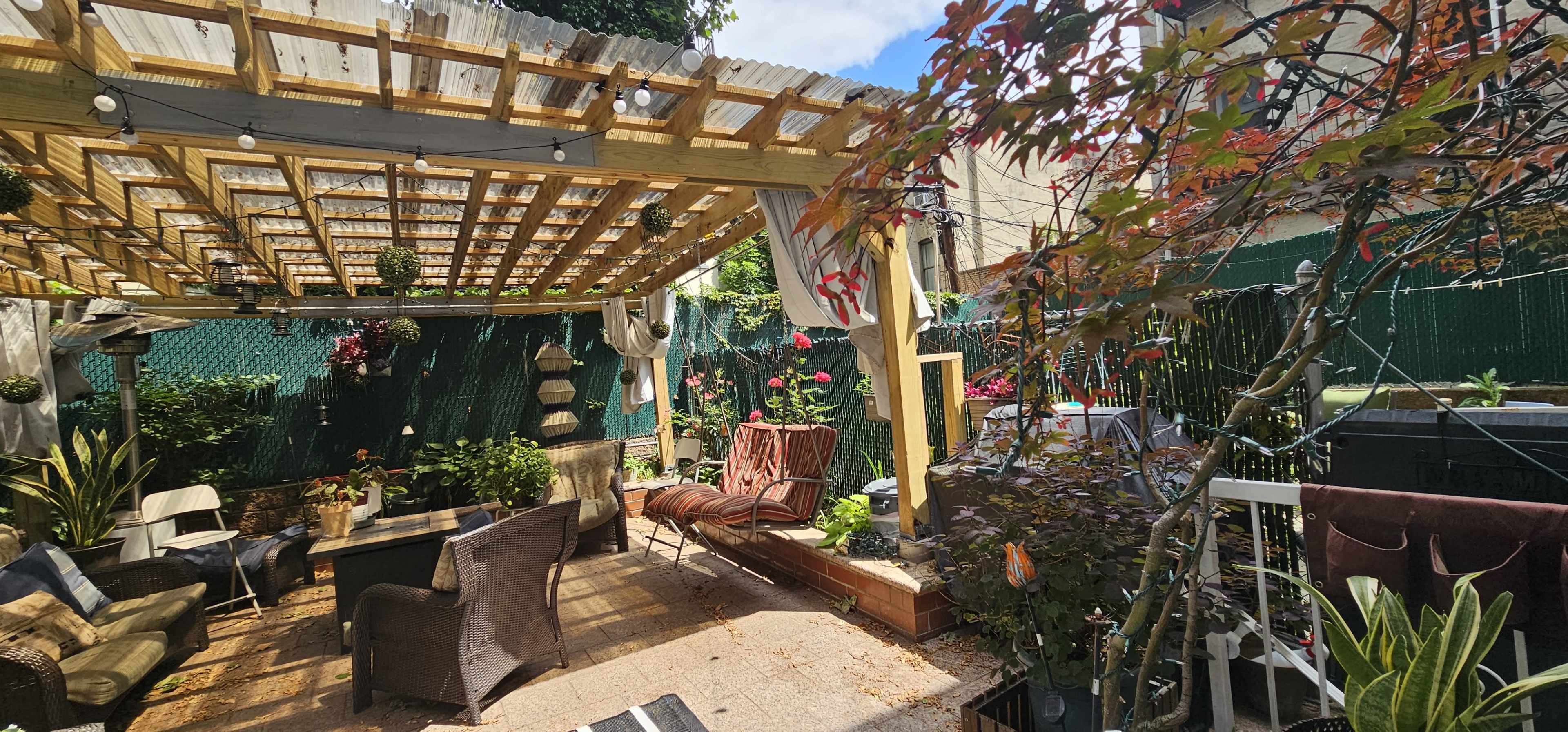 A cozy outdoor patio area with seating, plants, and a pergola covered in string lights.