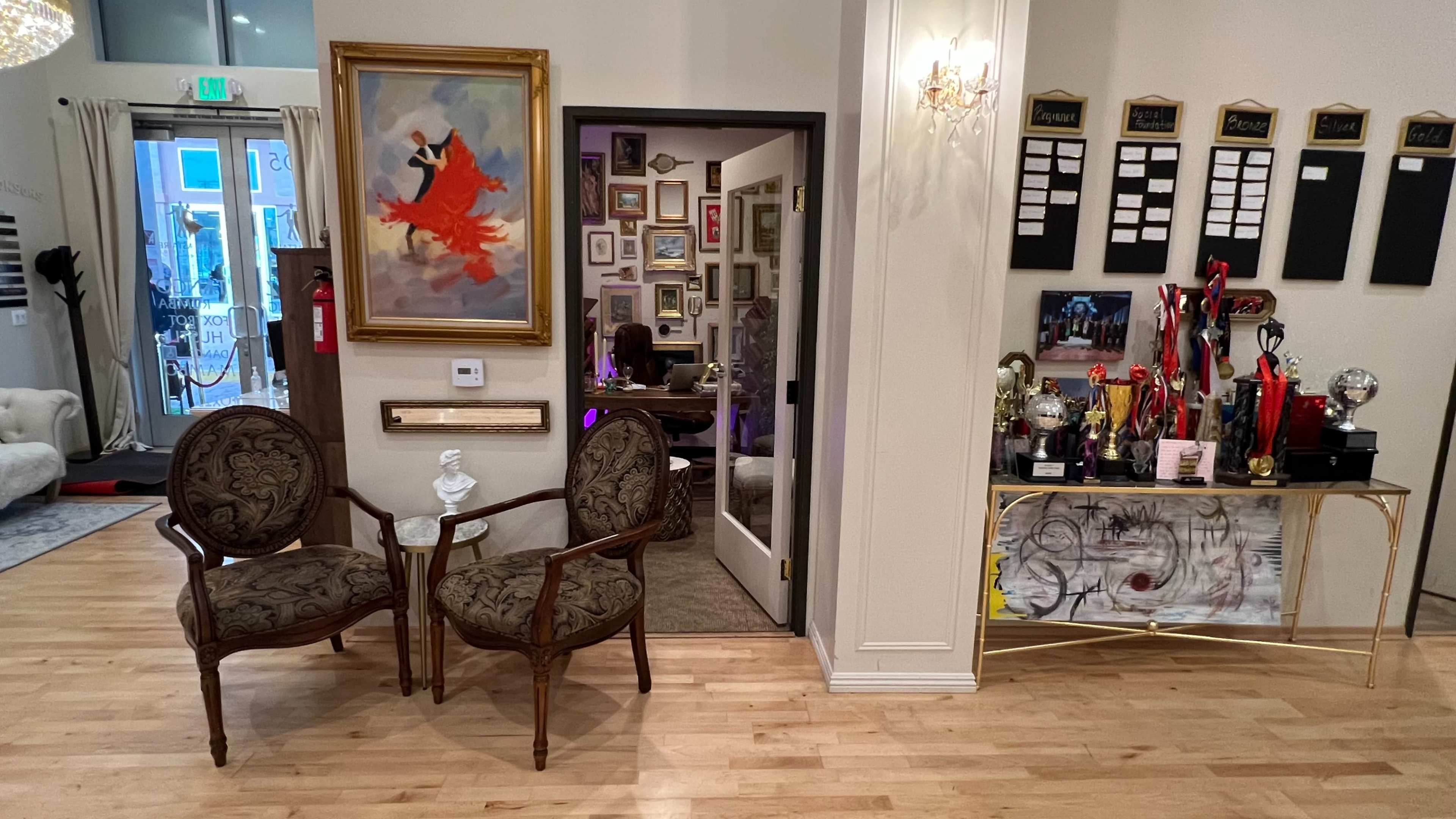 A well-decorated interior space featuring two chairs, a colorful painting on the wall, and a display of awards and trophies on a table.