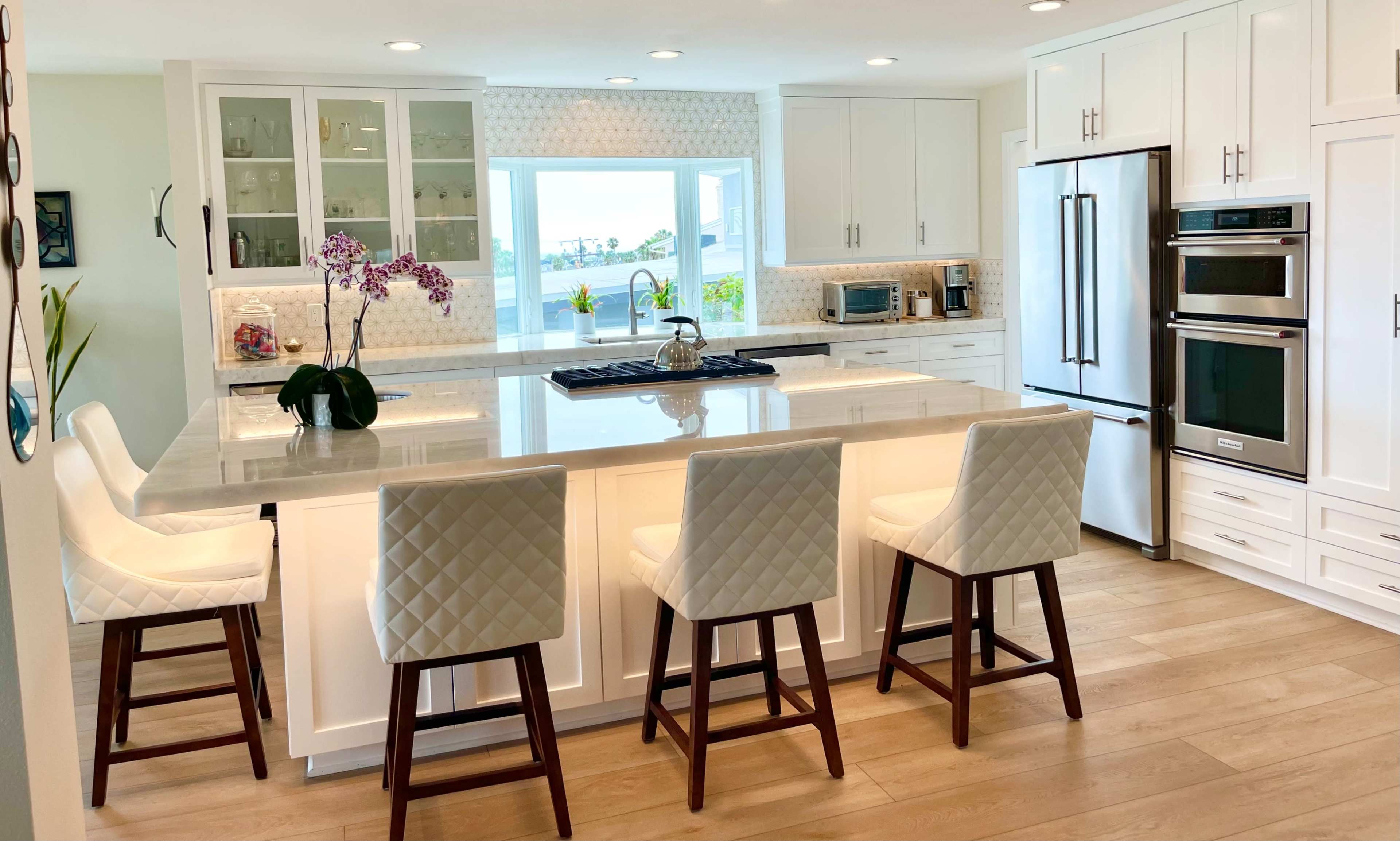 A modern kitchen with white cabinetry, a large island with seating for four, and a window overlooking an outdoor view.