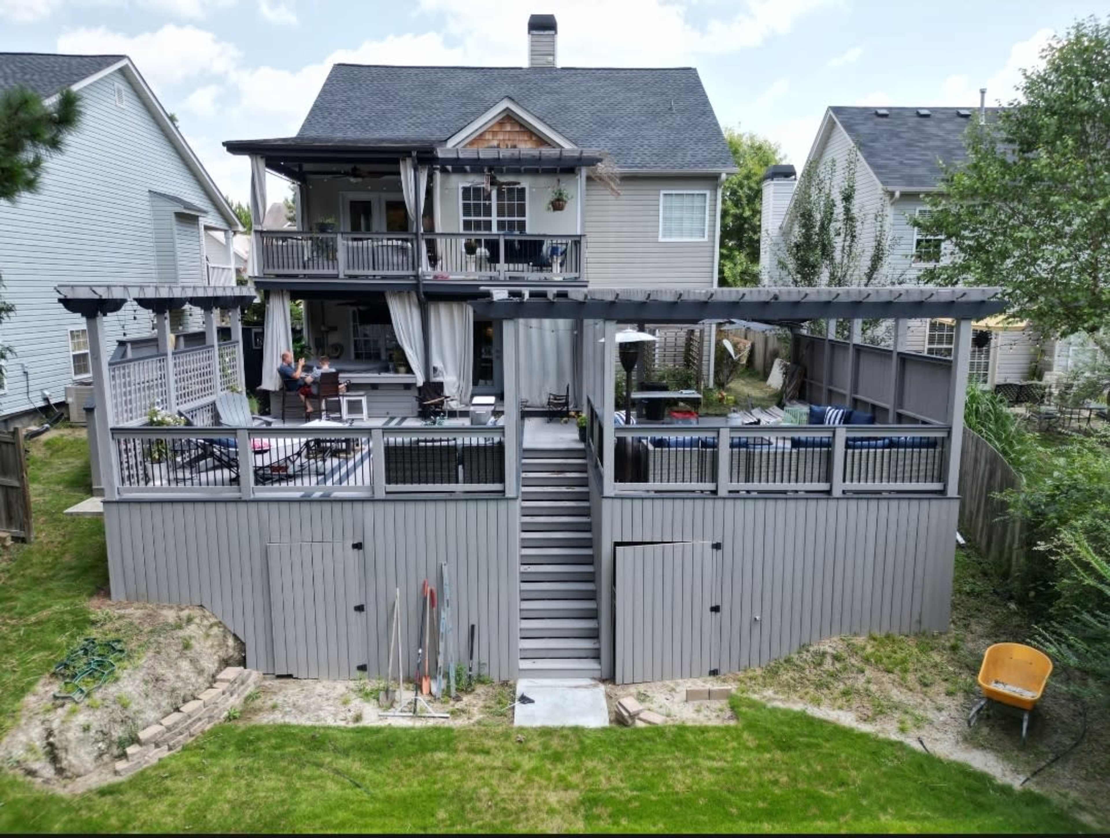 A two-story house with a large backyard deck, featuring multiple seating areas and staircases leading to the ground level.