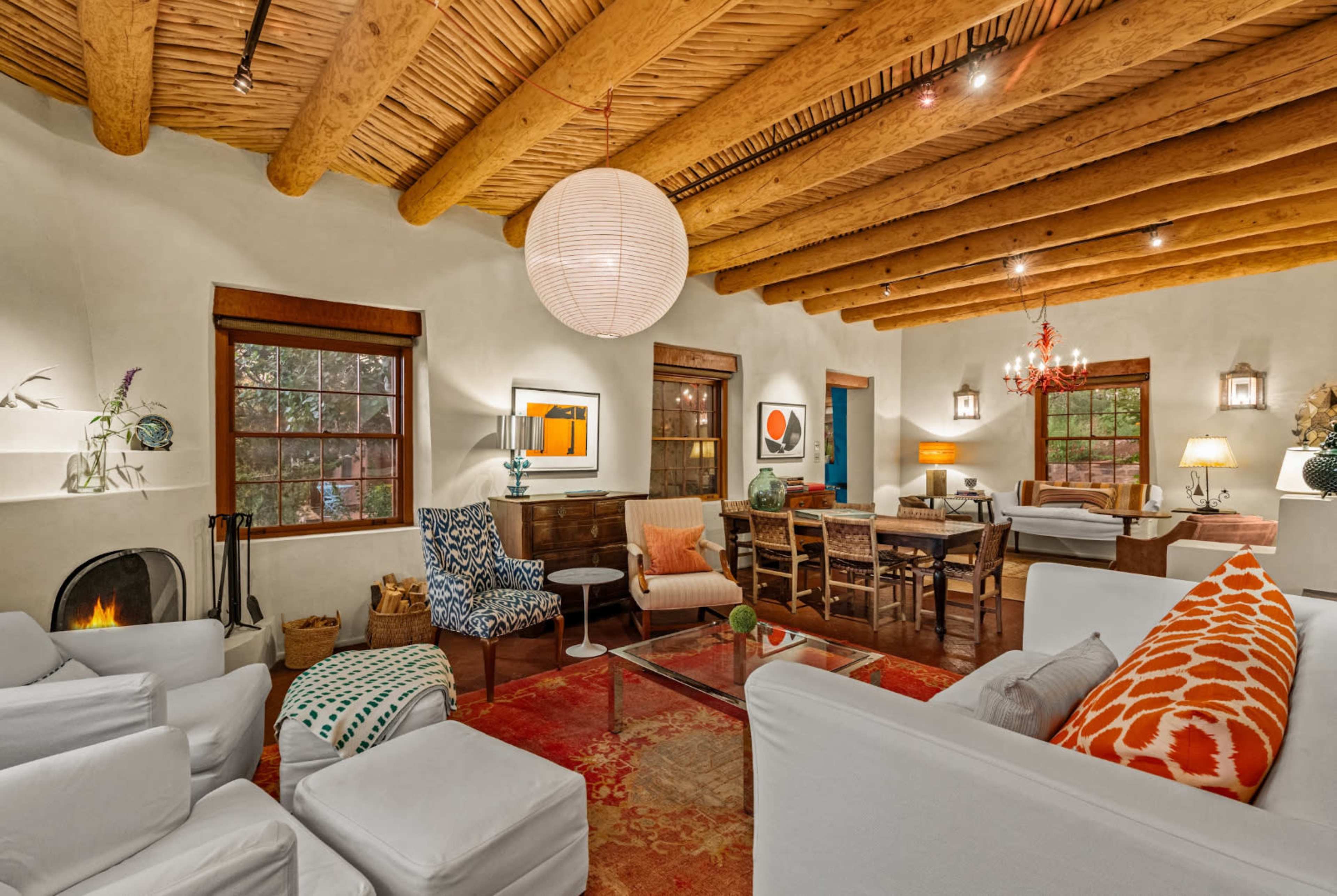 The living room features a mix of furniture styles, exposed wooden beams, and large windows that allow natural light to fill the space.