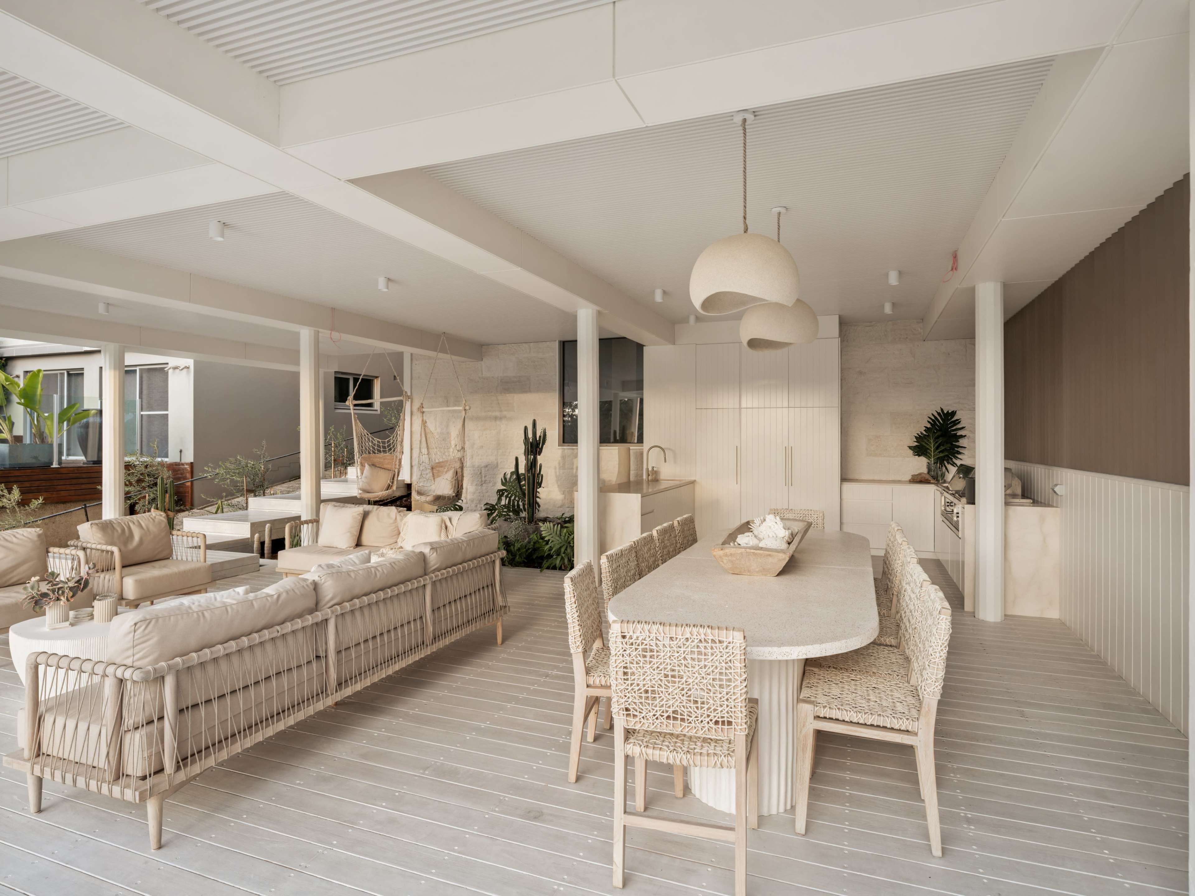 The image shows a modern, open-concept living space with a dining area, a comfortable sofa arrangement, and natural elements like plants and outdoor views.