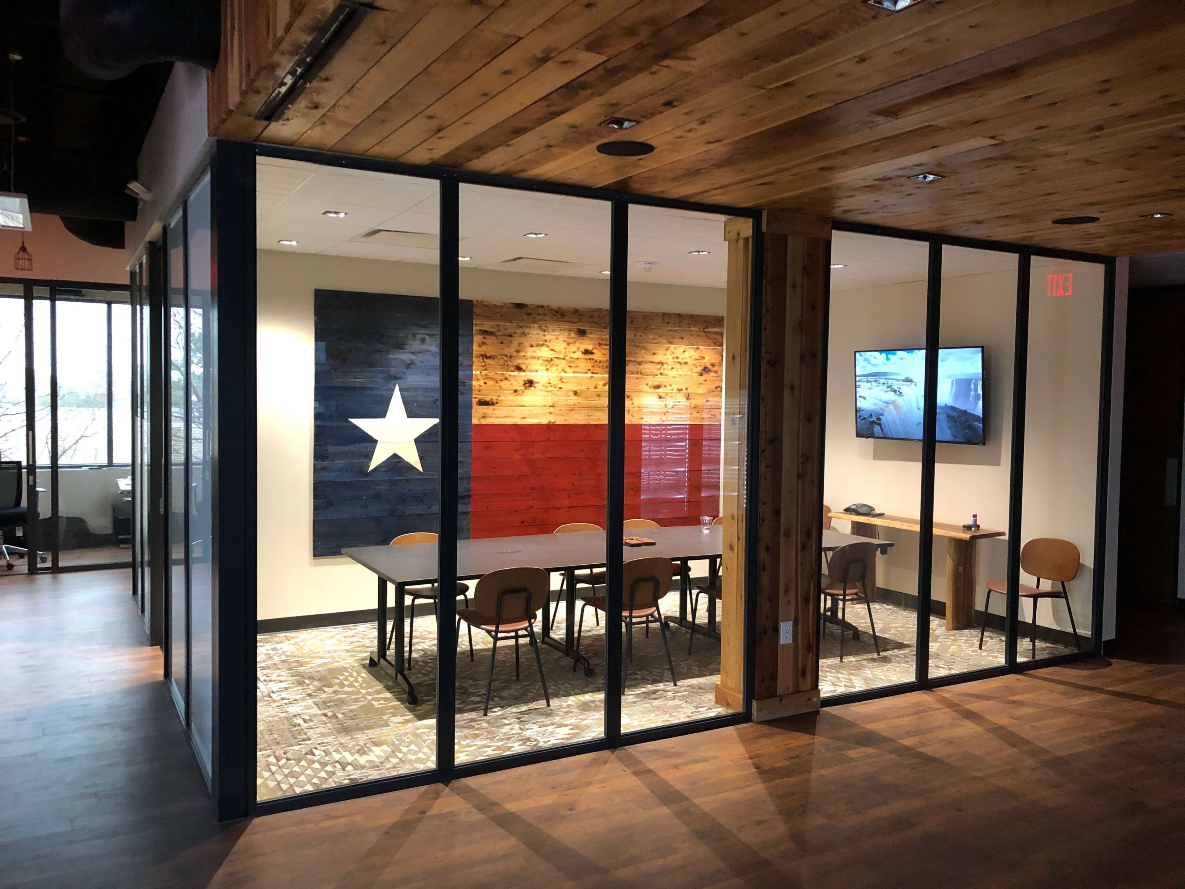 A conference room with glass walls featuring a large wooden wall art of the Texas flag and a television mounted on the side.