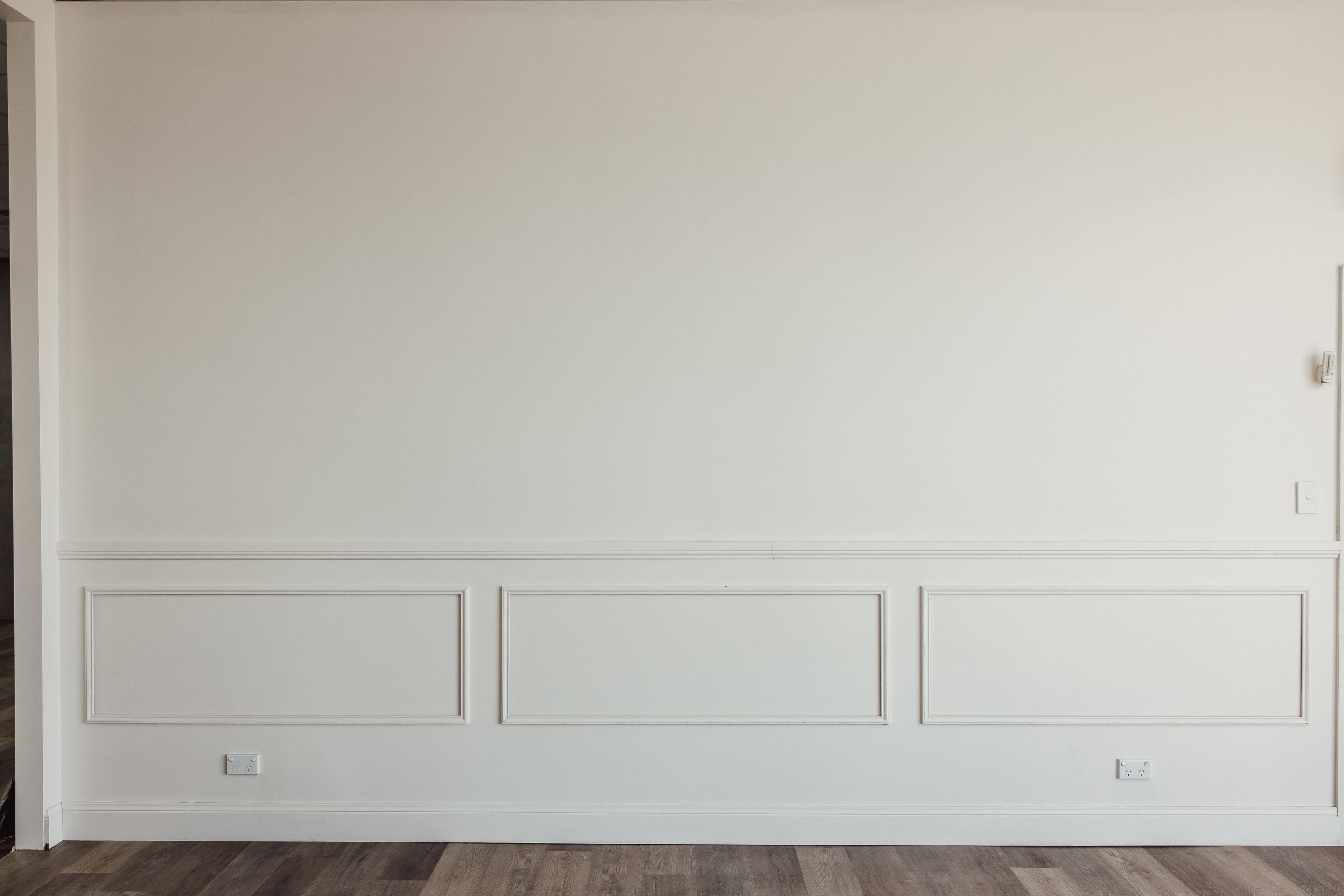 A plain white wall with decorative molding and wooden flooring.