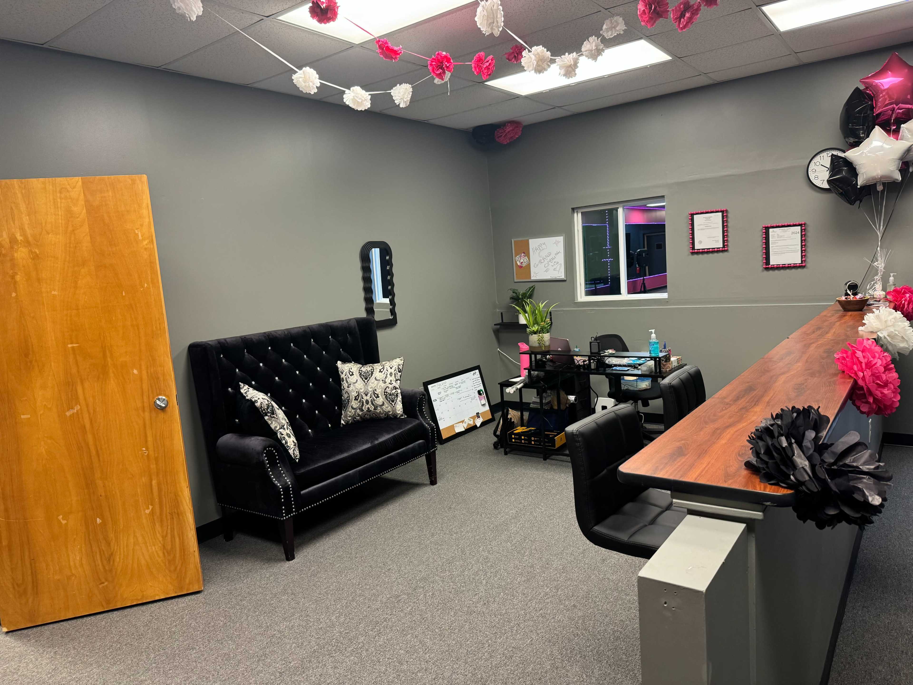 A reception area with a black tufted sofa, a wooden counter, chairs, and decorative flowers hanging from the ceiling.
