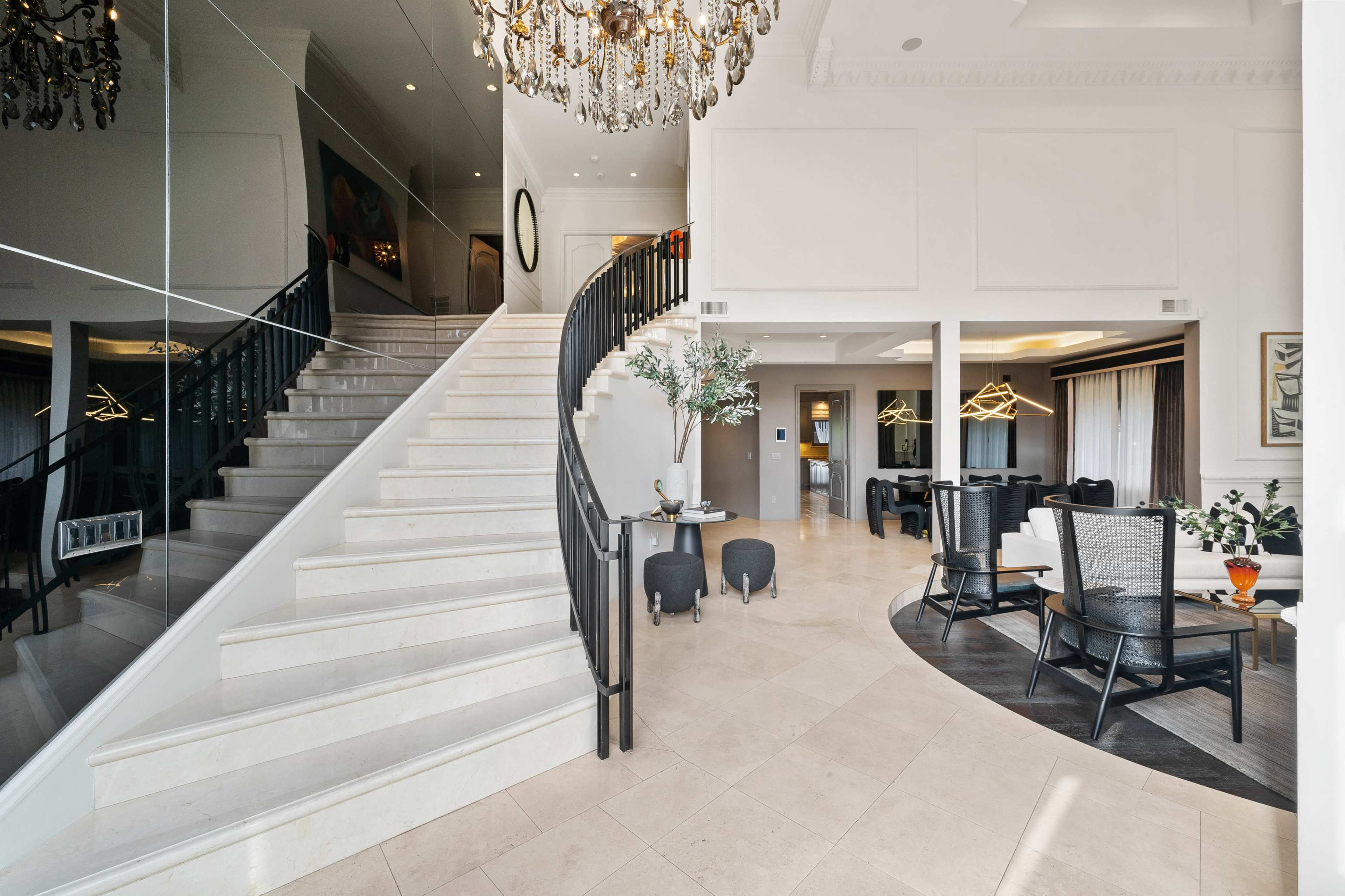 The image shows a spacious foyer with a curved staircase, a chandelier, and modern furniture arranged in a living area.