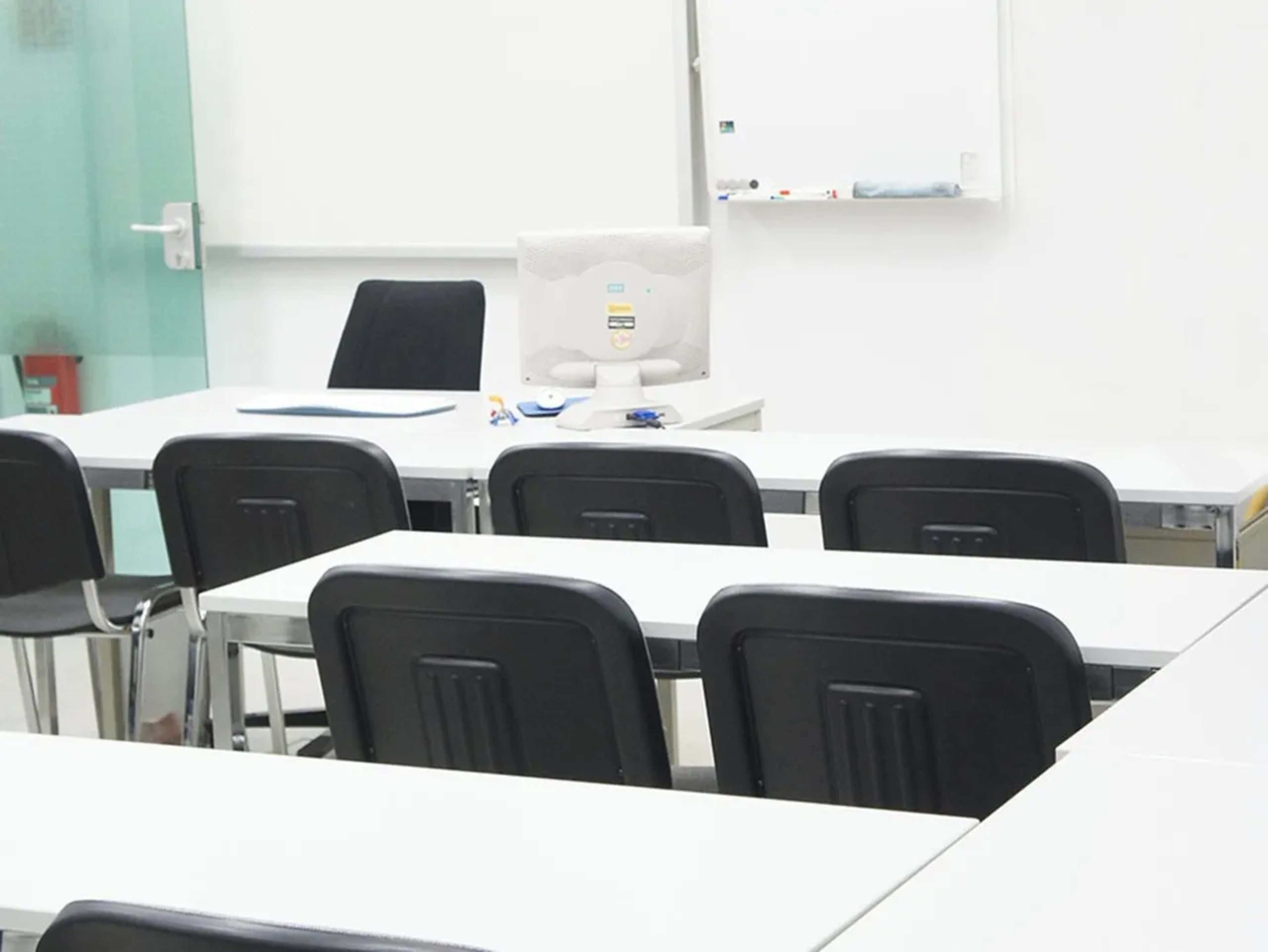 A classroom with empty desks and a computer setup facing a whiteboard.