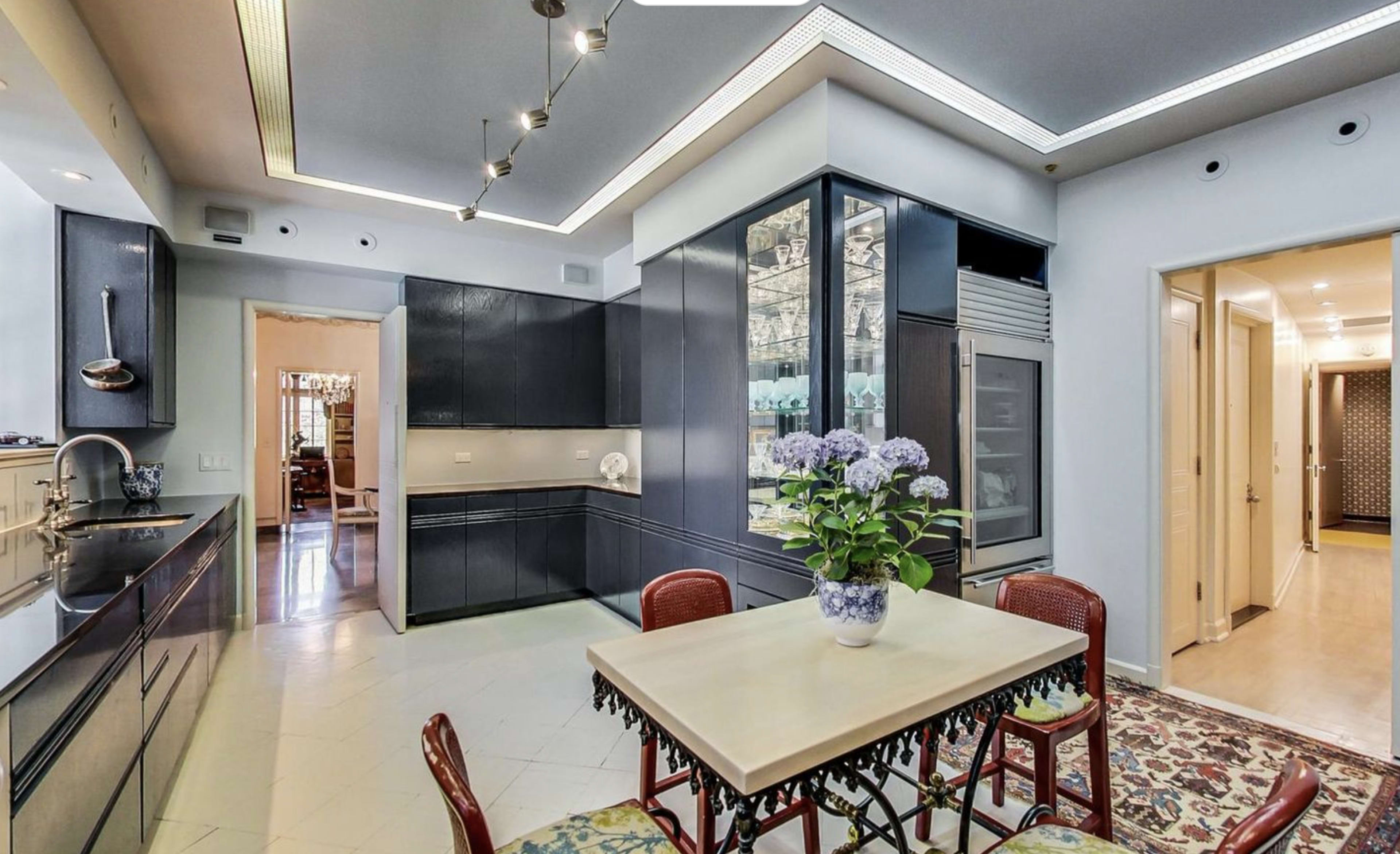 A modern kitchen with dark cabinetry, a central dining table, and a door leading to another room.