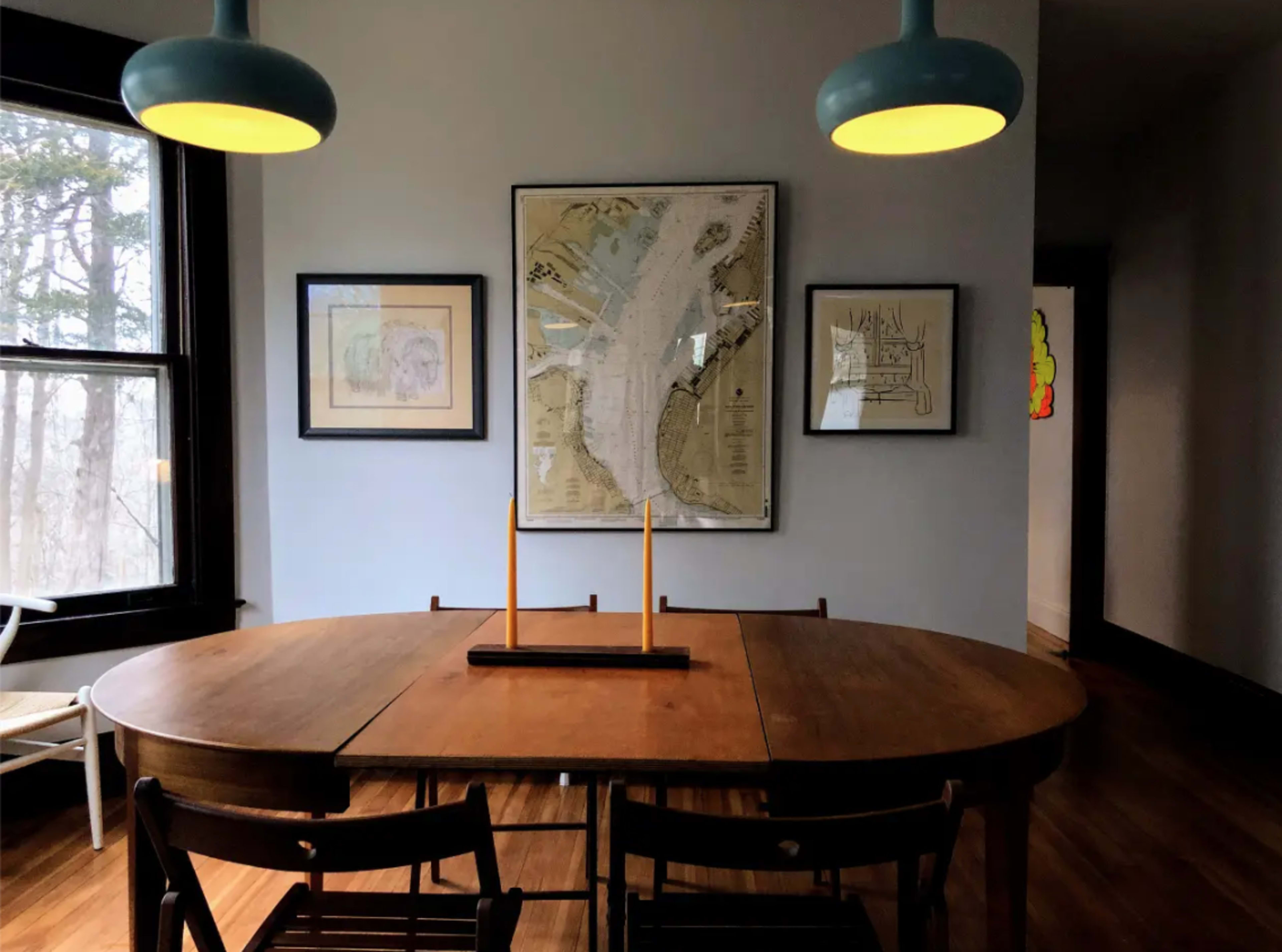 A dining area features a wooden table with chairs, illuminated by pendant lights, and is adorned with framed maps and artwork on the walls.