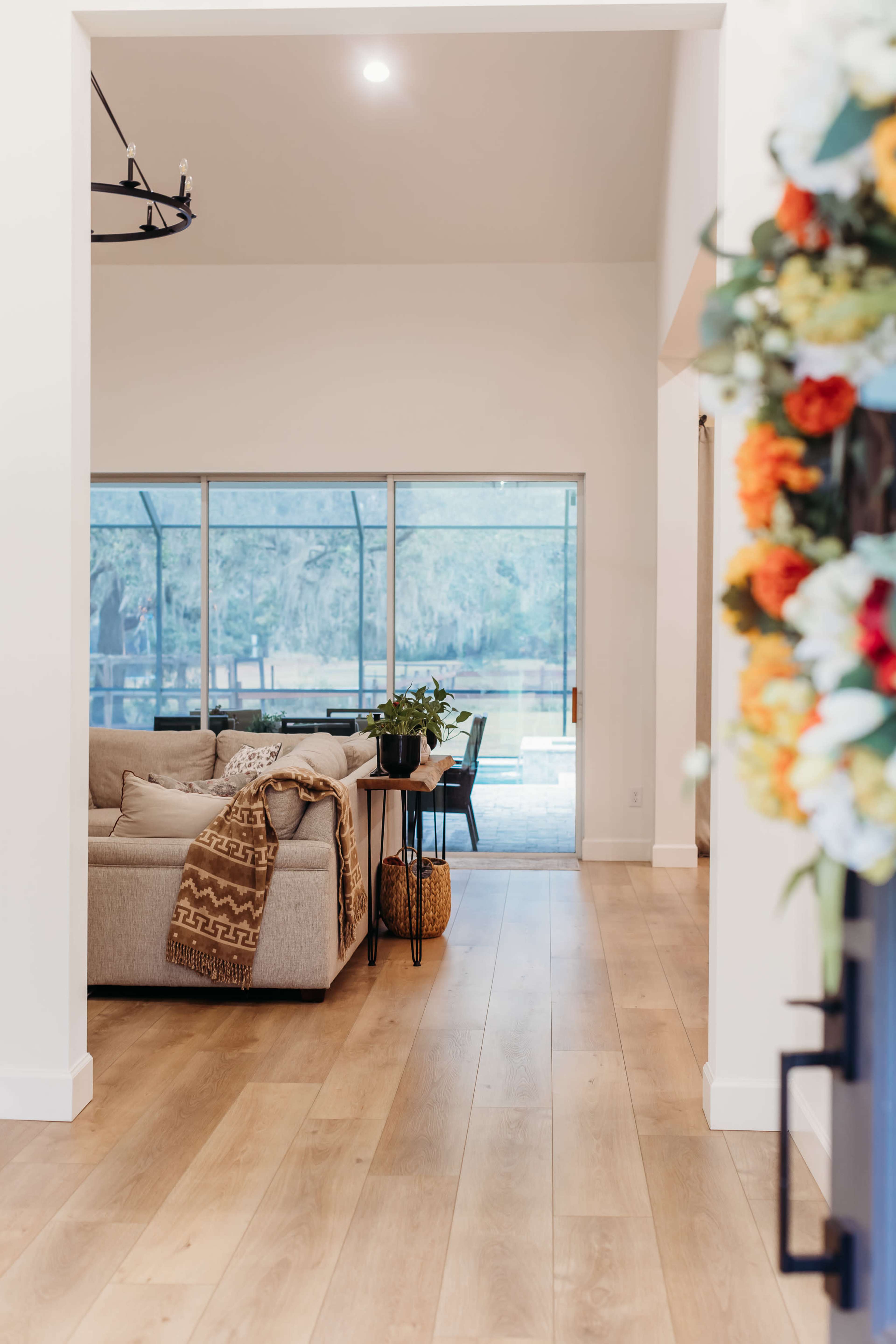 A spacious living area features a light-colored sofa, a dining table, and large windows overlooking a patio.