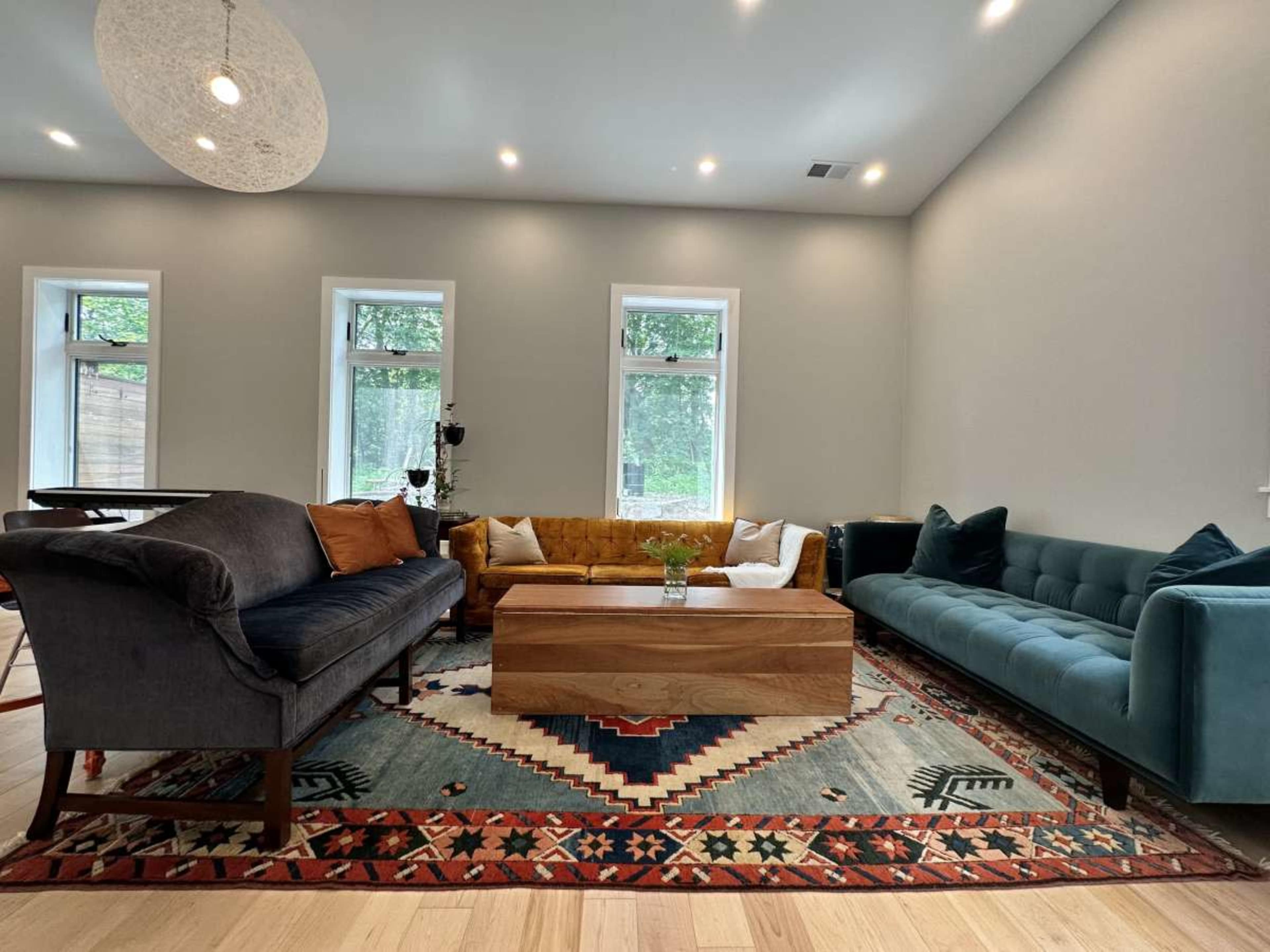 The living room features a mix of seating options, including a gray sofa, a mustard yellow couch, and a teal tufted loveseat, arranged around a wooden coffee table on a patterned rug.
