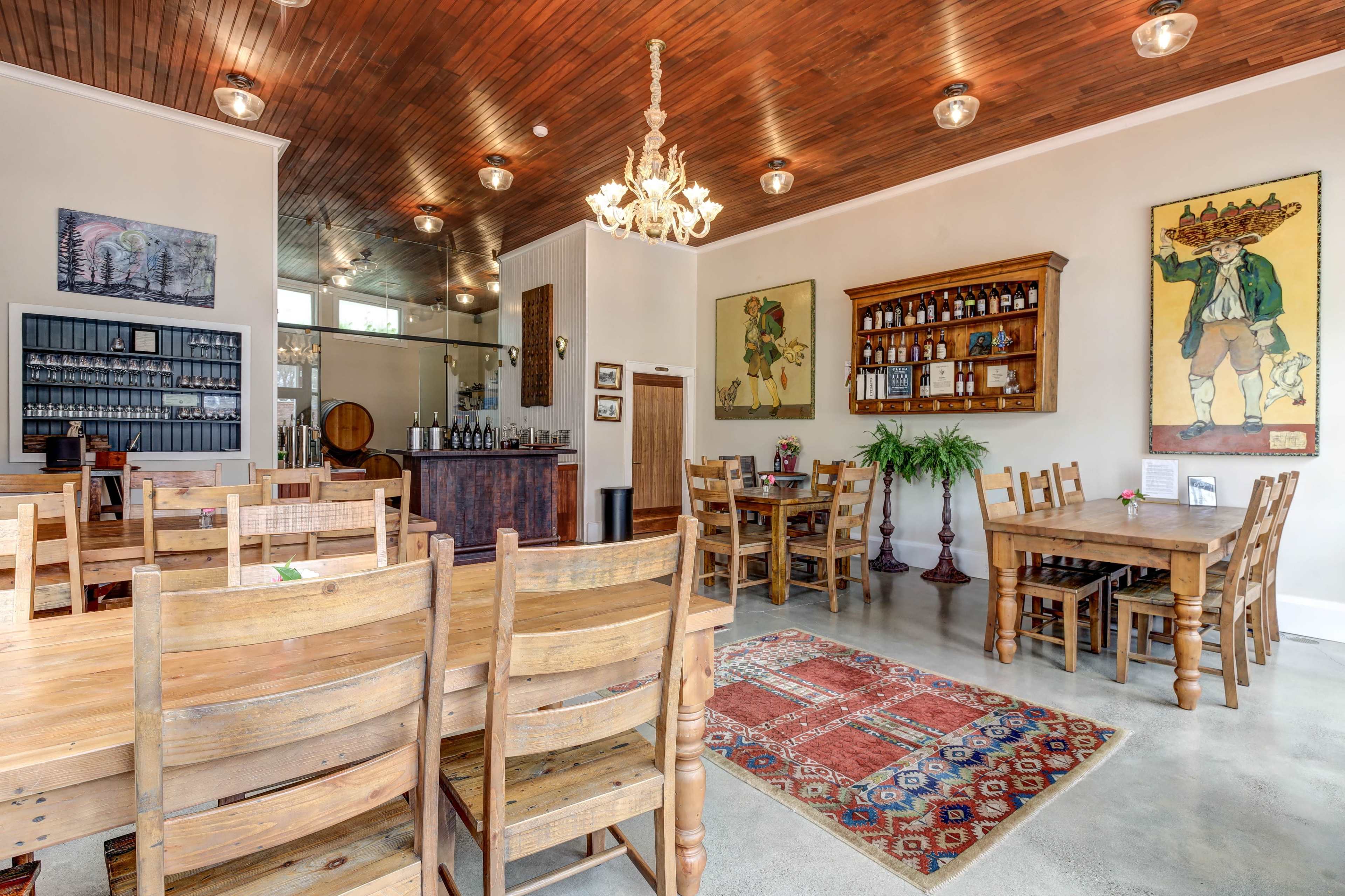 The image shows the interior of a restaurant featuring wooden furniture, a bar area, and decorative artwork on the walls.