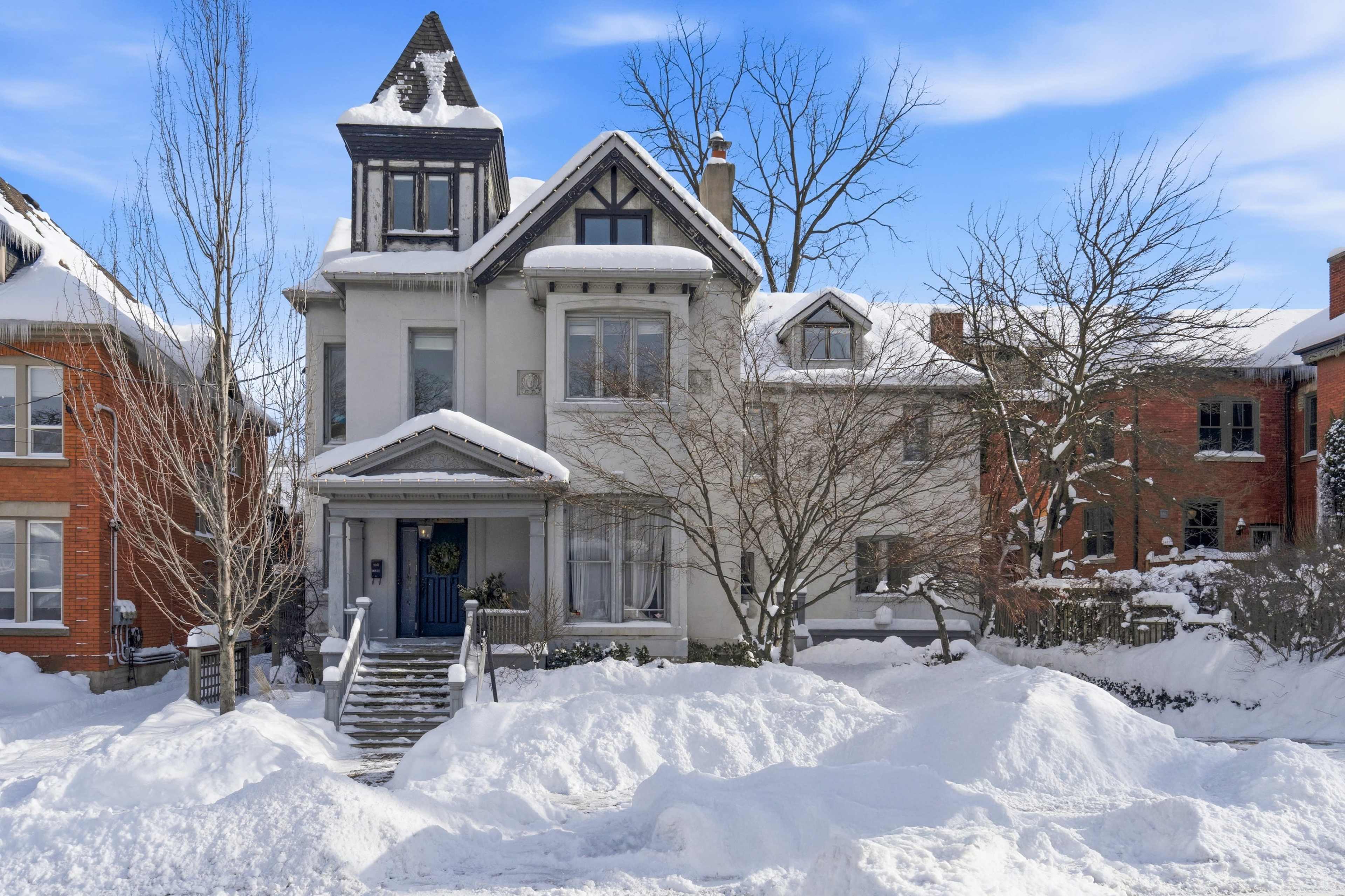 A large, historic house with a pointed roof stands surrounded by snow-covered lawns and trees.