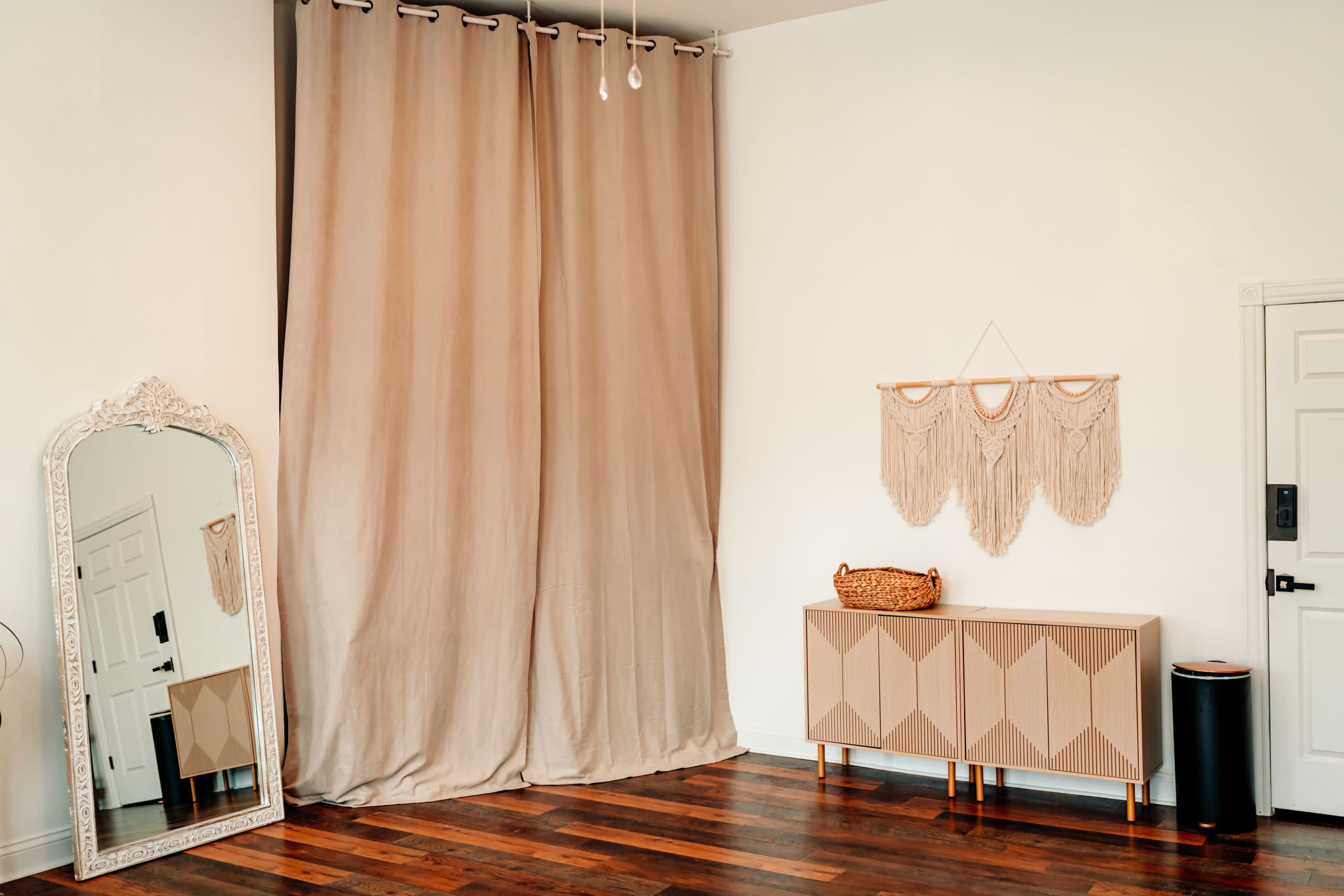 The scene features a spacious room with a large mirror, floor-length curtains, a patterned cabinet, and a decorative wall hanging.