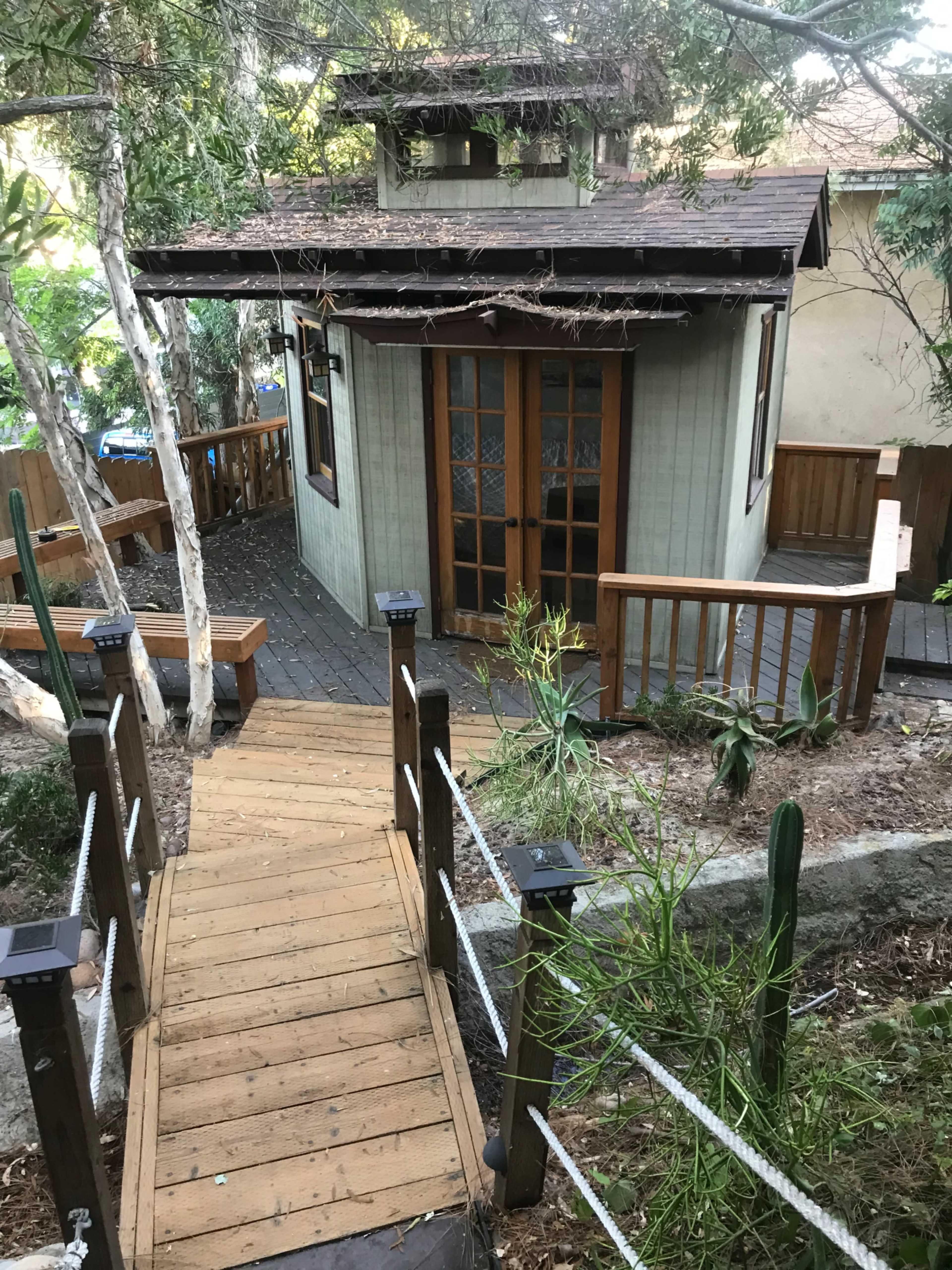 A wooden pathway leads to a small, cottage-style structure surrounded by greenery.