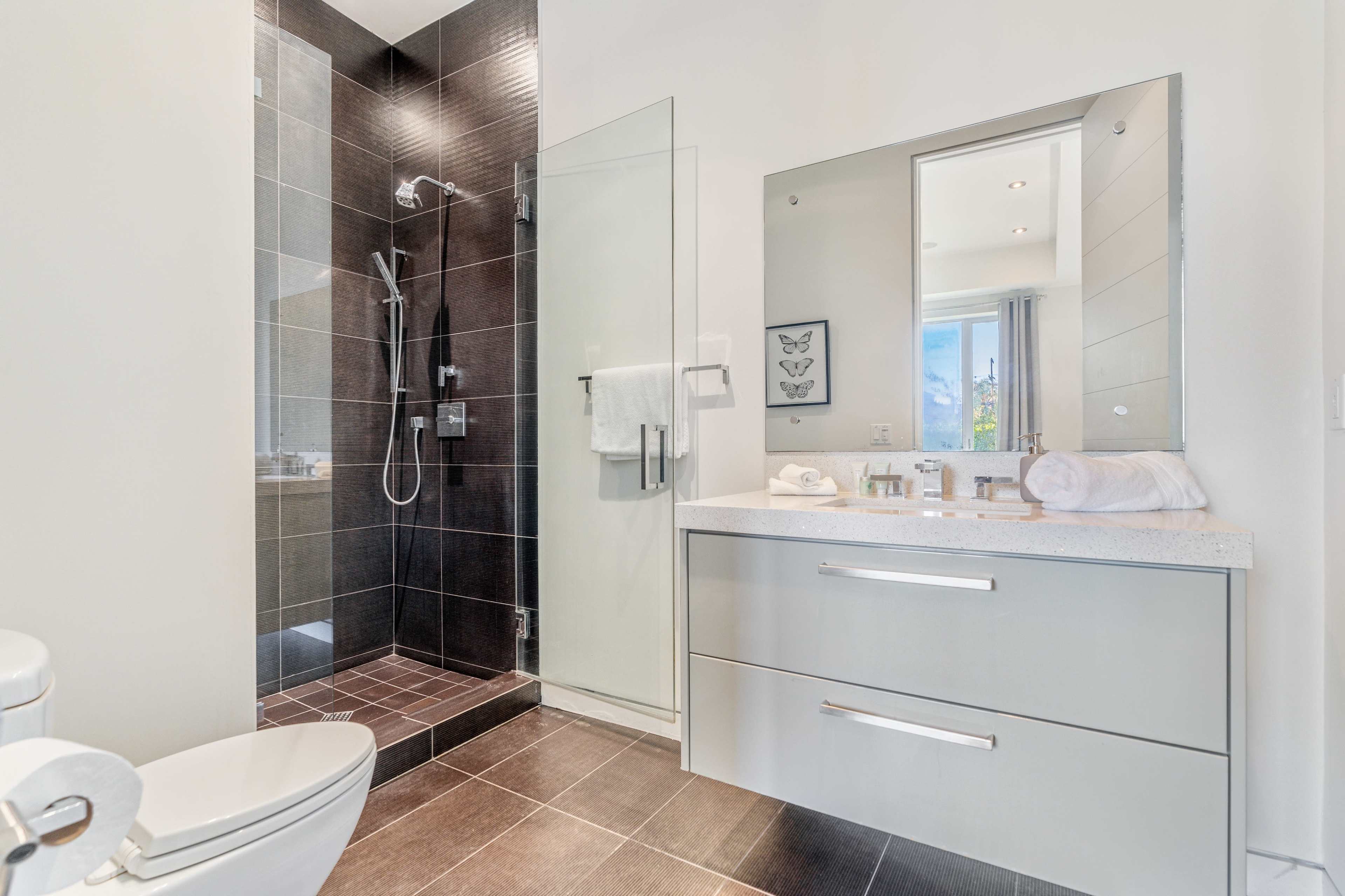 A modern bathroom featuring a walk-in shower, a single vanity with a large mirror, and a toilet.