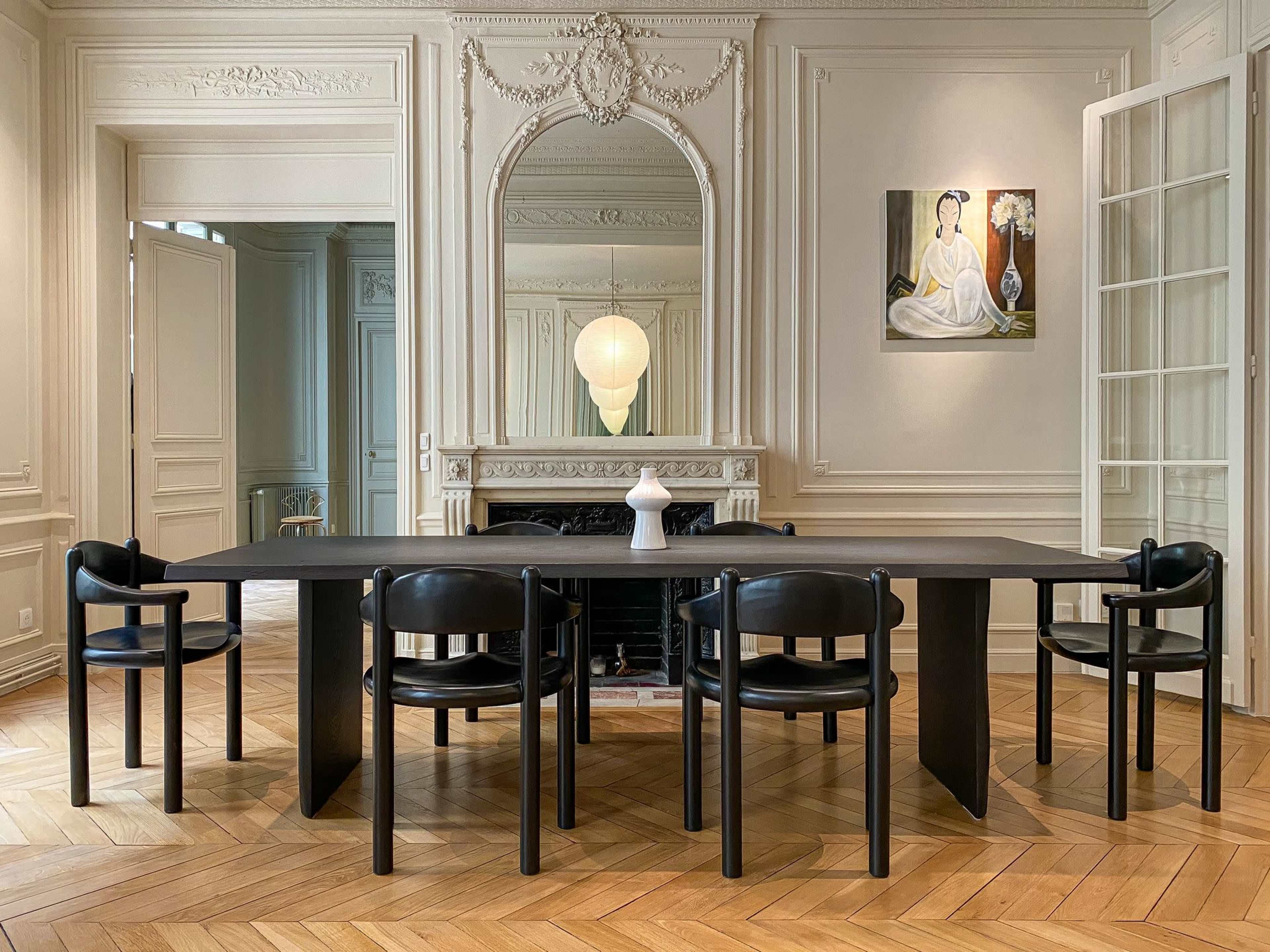 The image shows a modern dining room featuring a long black table surrounded by black chairs, with a large mirror and artwork on the walls.
