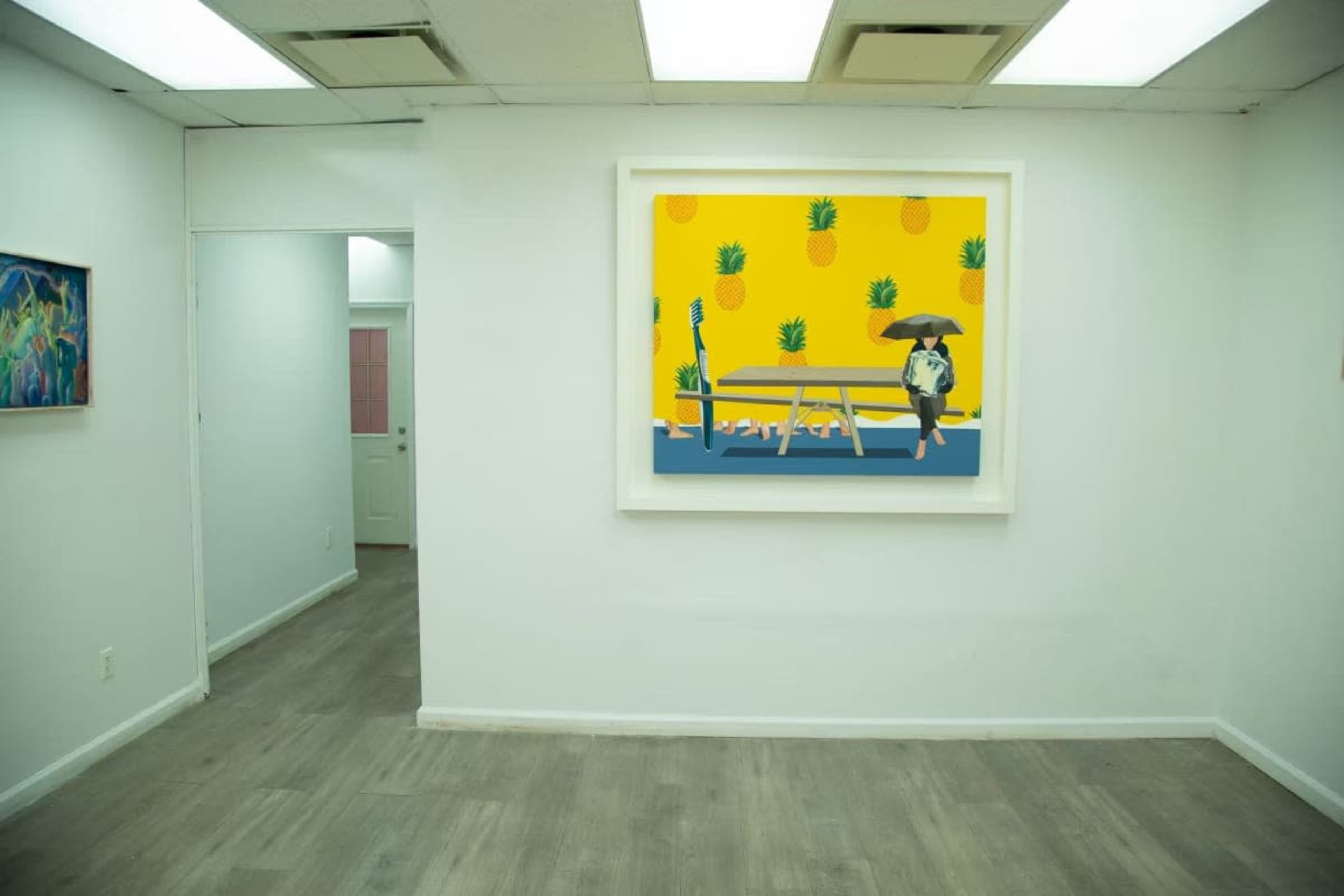 The image shows a bright, minimalist gallery space with white walls, featuring a large artwork of a dog with a hat sitting on a bench in a pineapple-themed setting.