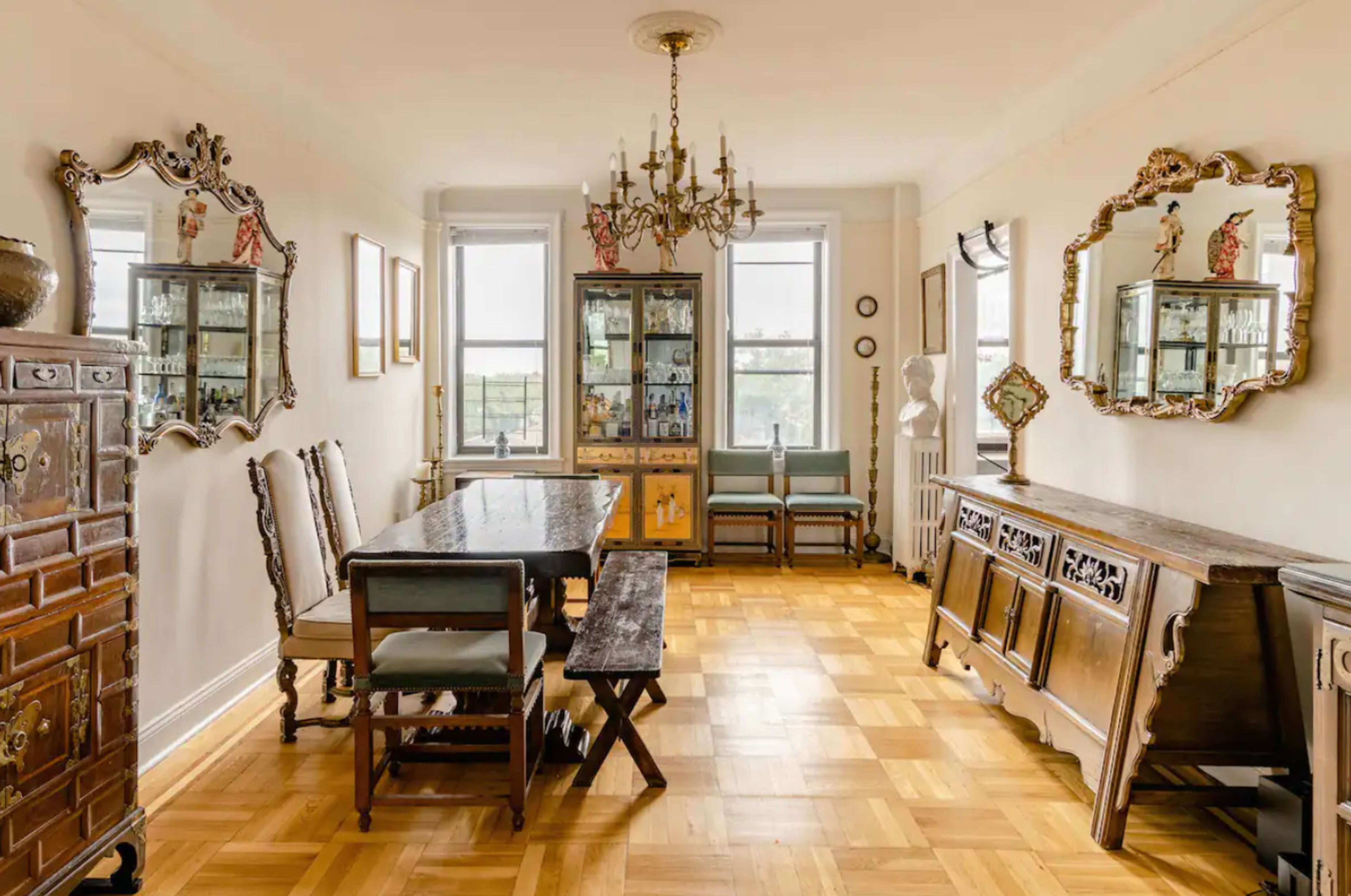 The room features a dining area with a wooden table, surrounded by chairs, and adorned with mirrored wall decor and a chandelier overhead.