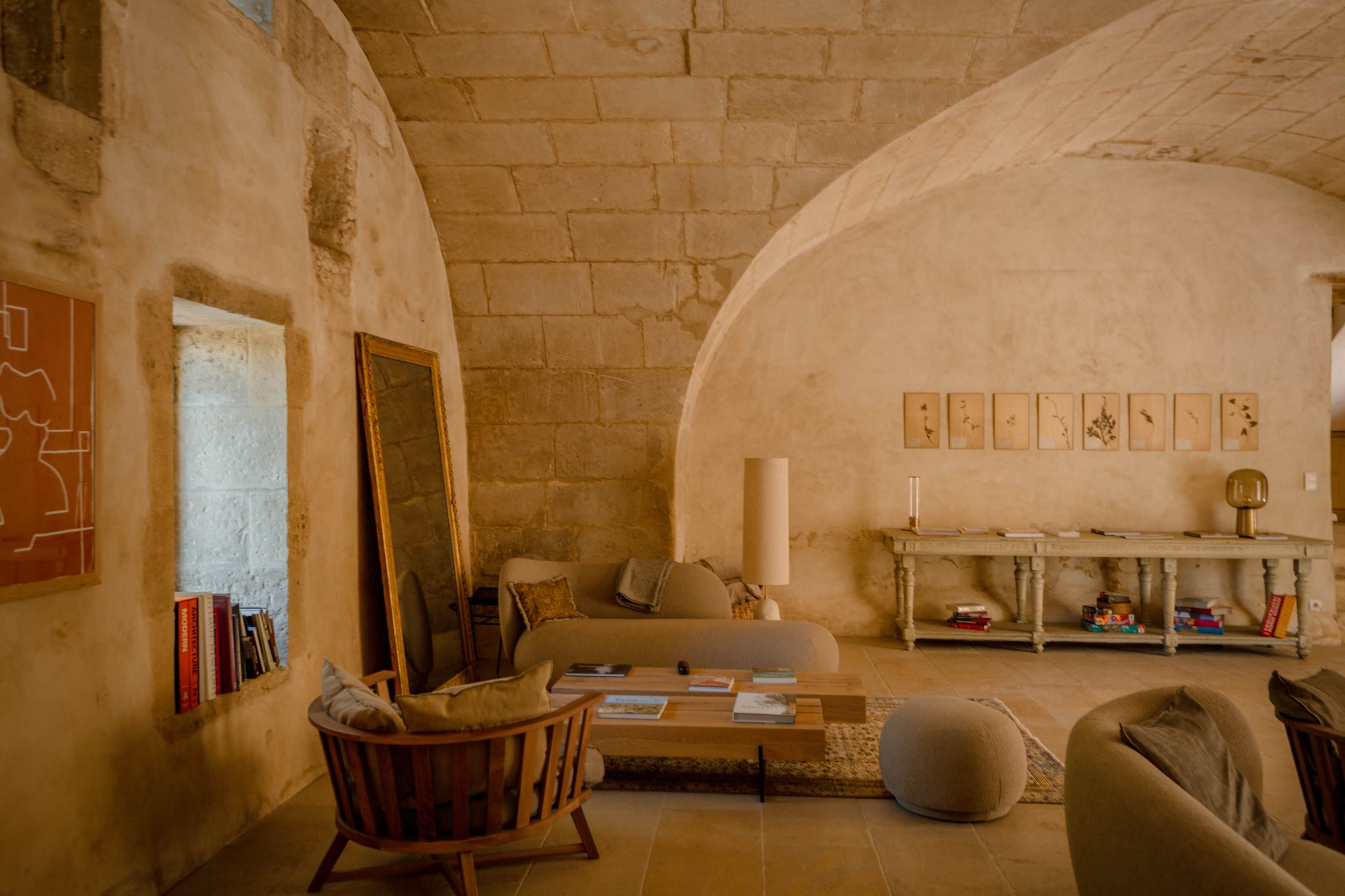 The image shows a spacious interior with arched stone walls, featuring a seating area with modern furniture, a coffee table, and decorative wall art.